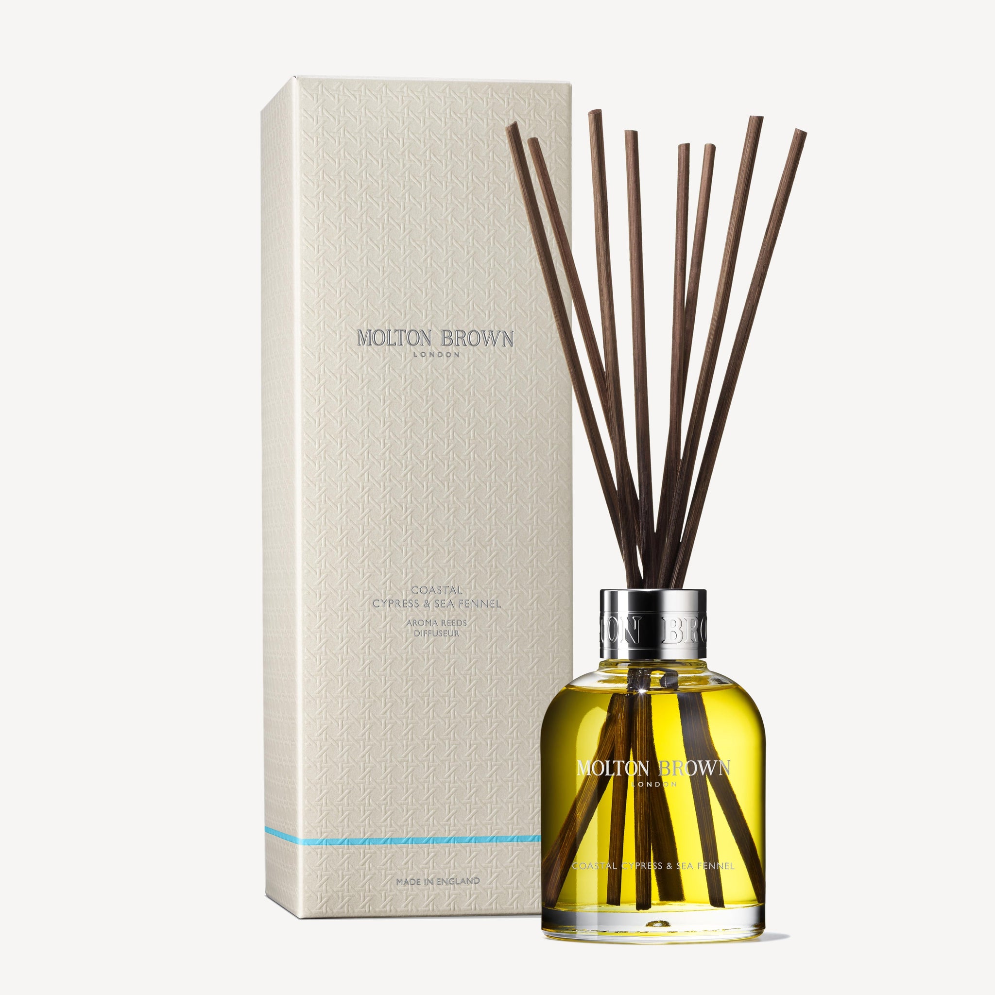 The Coastal Cypress & Sea Fennel Aroma Reeds 150ml by MoltonBrown Cyprus, showcasing an aromatic fragrance, is depicted with a glass bottle filled with yellow liquid and several aroma reeds next to the packaging box.