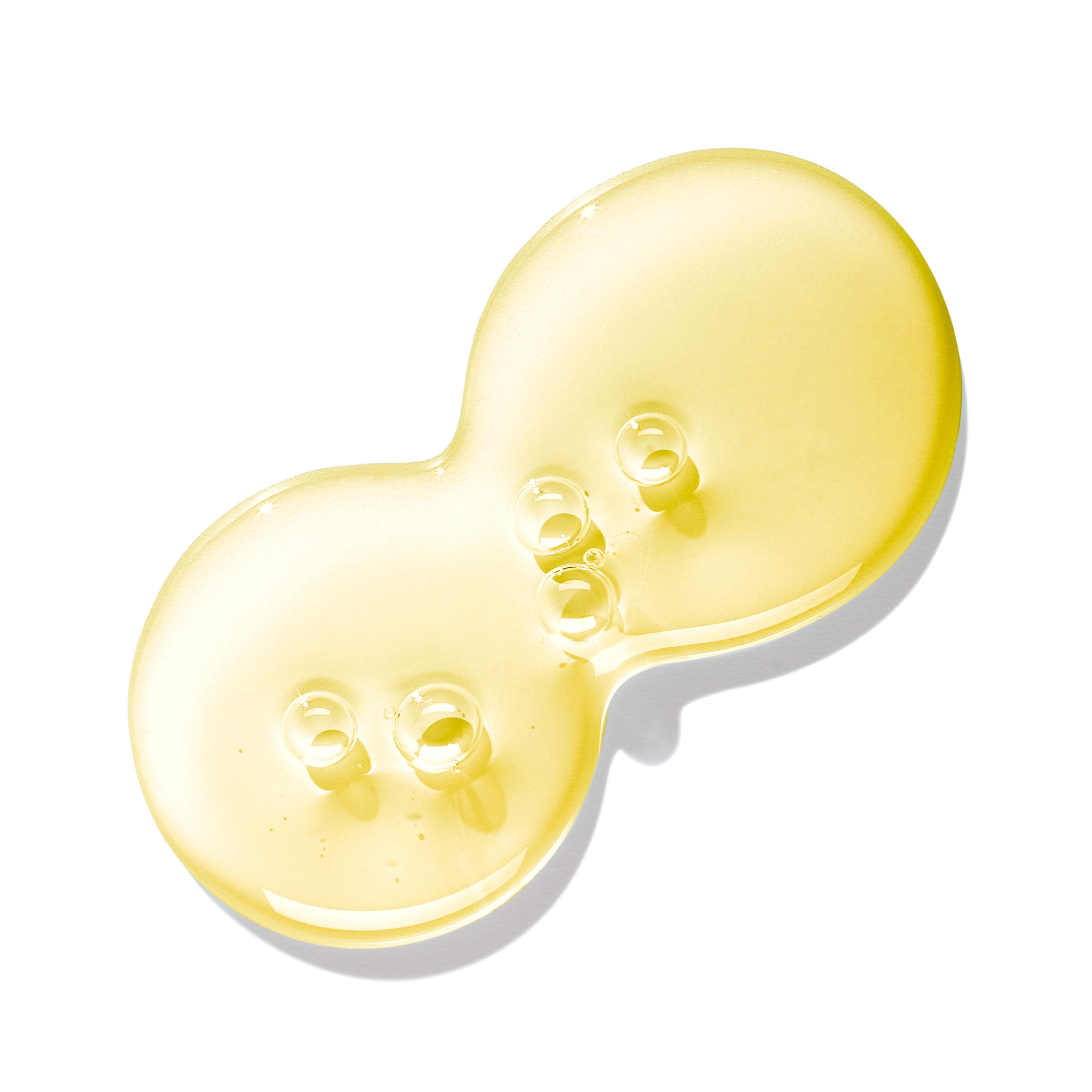 A golden, glossy liquid forms a peanut-shaped puddle on a white background, with small bubbles hinting at the essence of jasmine and honeysuckle swirling within, evoking the luxurious blend of MoltonBrown Cyprus's Purifying Shampoo With Indian Cress 300ml.