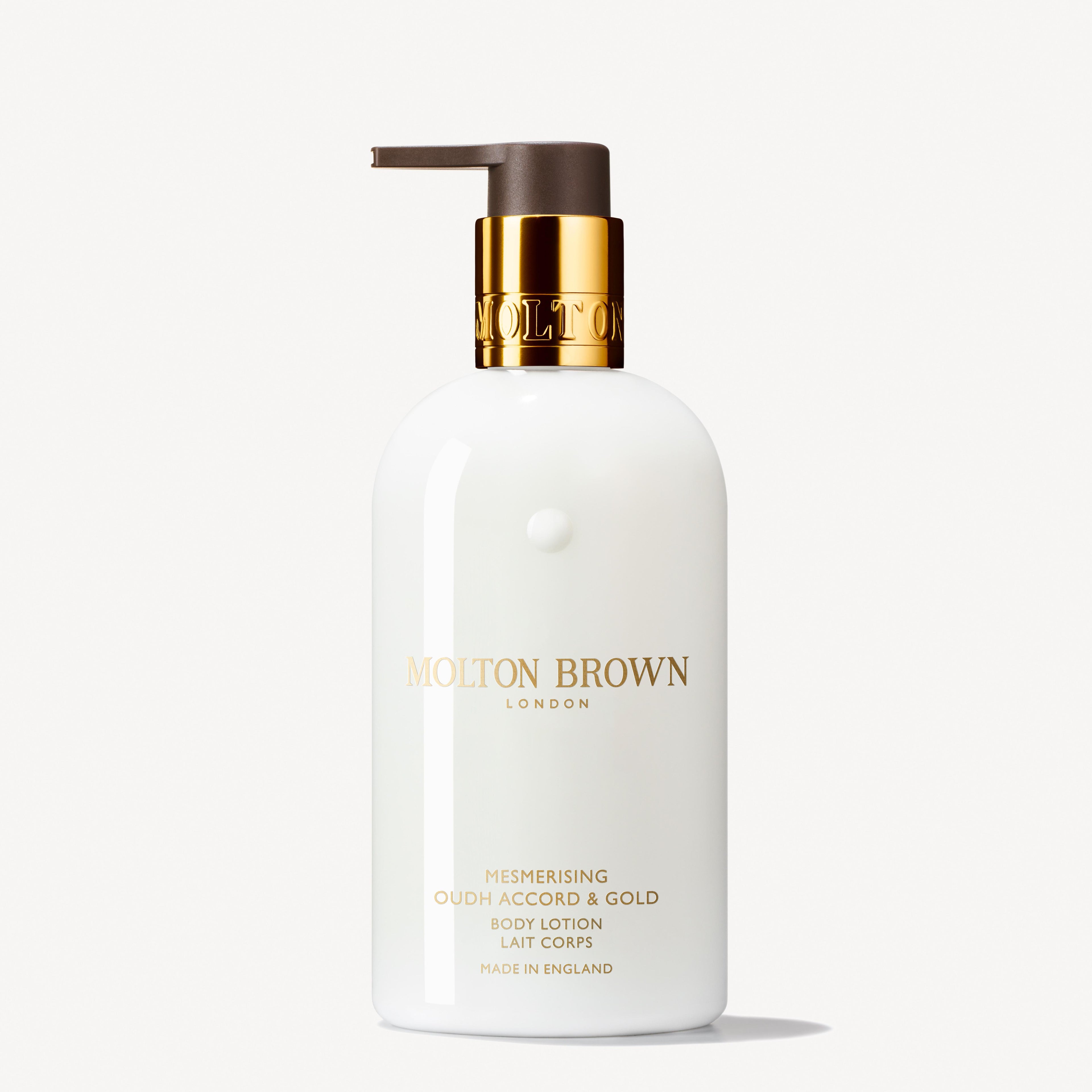 A MoltonBrown Cyprus body lotion, elegantly labeled as the Mesmerising Oudh Accord & Gold Body Lotion 300ml, features a sleek white bottle with a gold pump and brown cap that exudes luxury while highlighting its enchanting blend of oudh and myrrh in sophisticated text and branding.