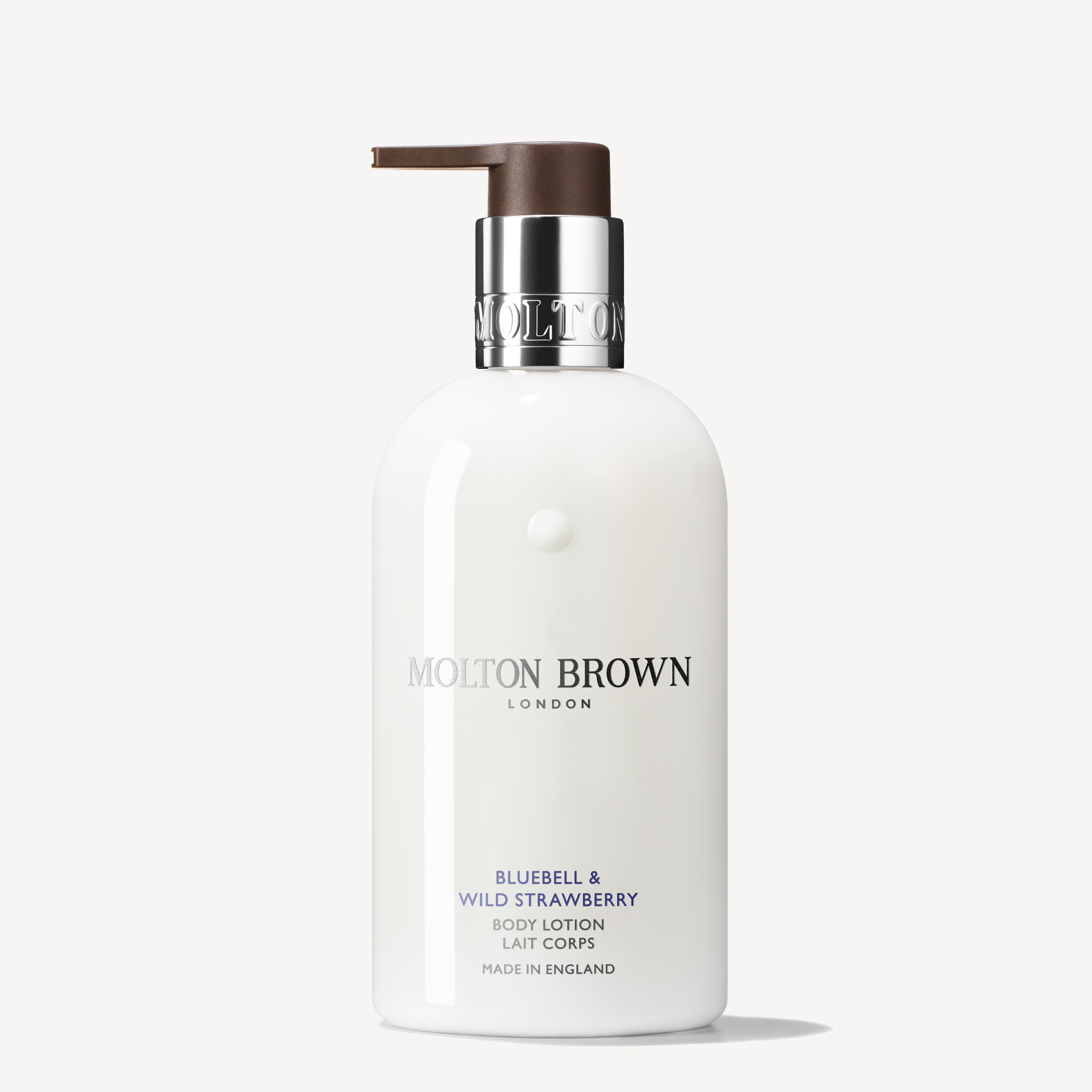 A white bottle of Bluebell & Wild Strawberry Body Lotion by MoltonBrown Cyprus, featuring a brown pump dispenser, exudes a floral-fruity scent. The brand logo and product details shimmer in silver and purple against the white background.