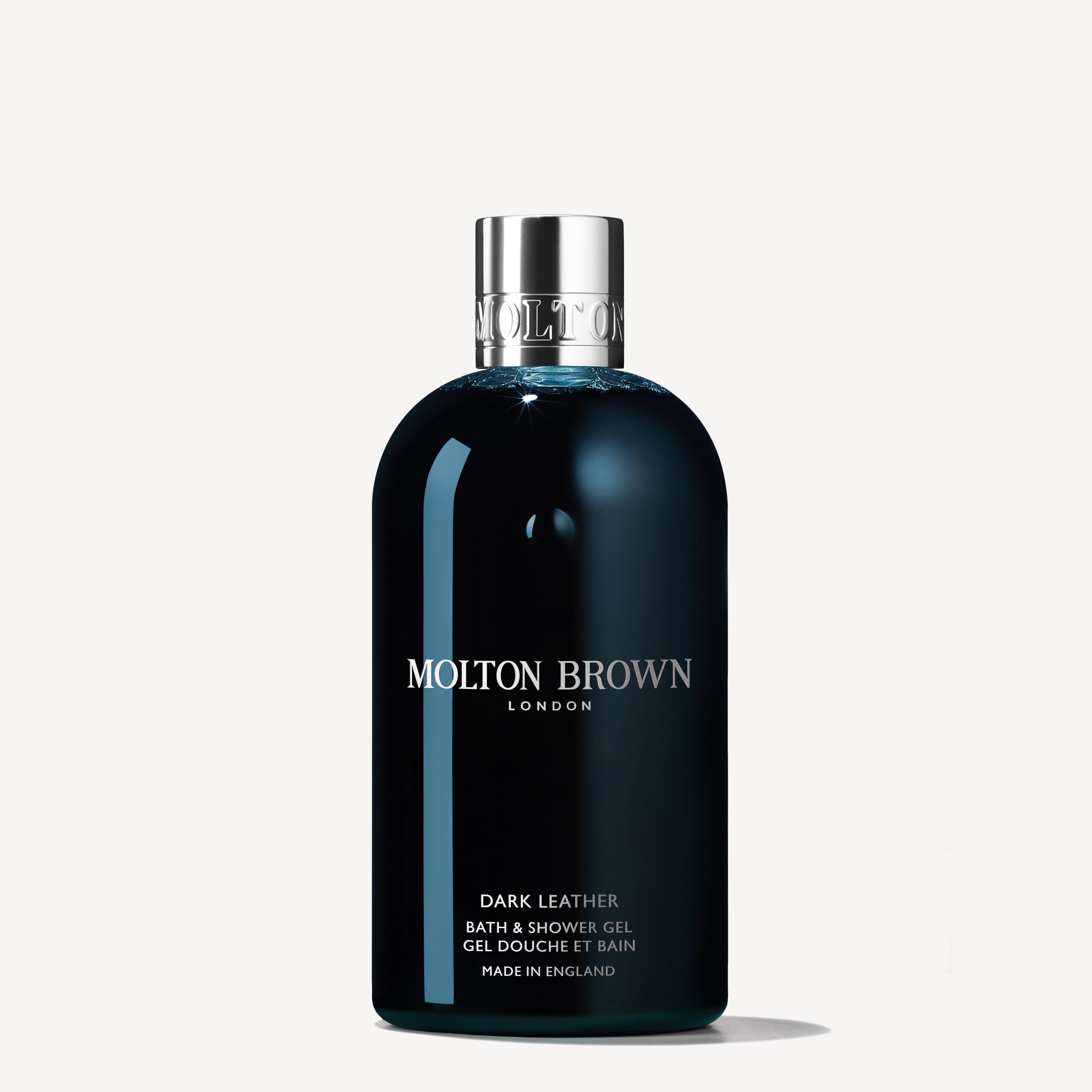 A 300ml bottle of MoltonBrown Cyprus Dark Leather Bath & Shower Gel, featuring a chrome cap, exudes sophistication. Its black label with white text prominently displays the brand's logo and product details, while notes of aged leather and a subtle tobacco accord enhance this luxurious experience against an off-white backdrop.