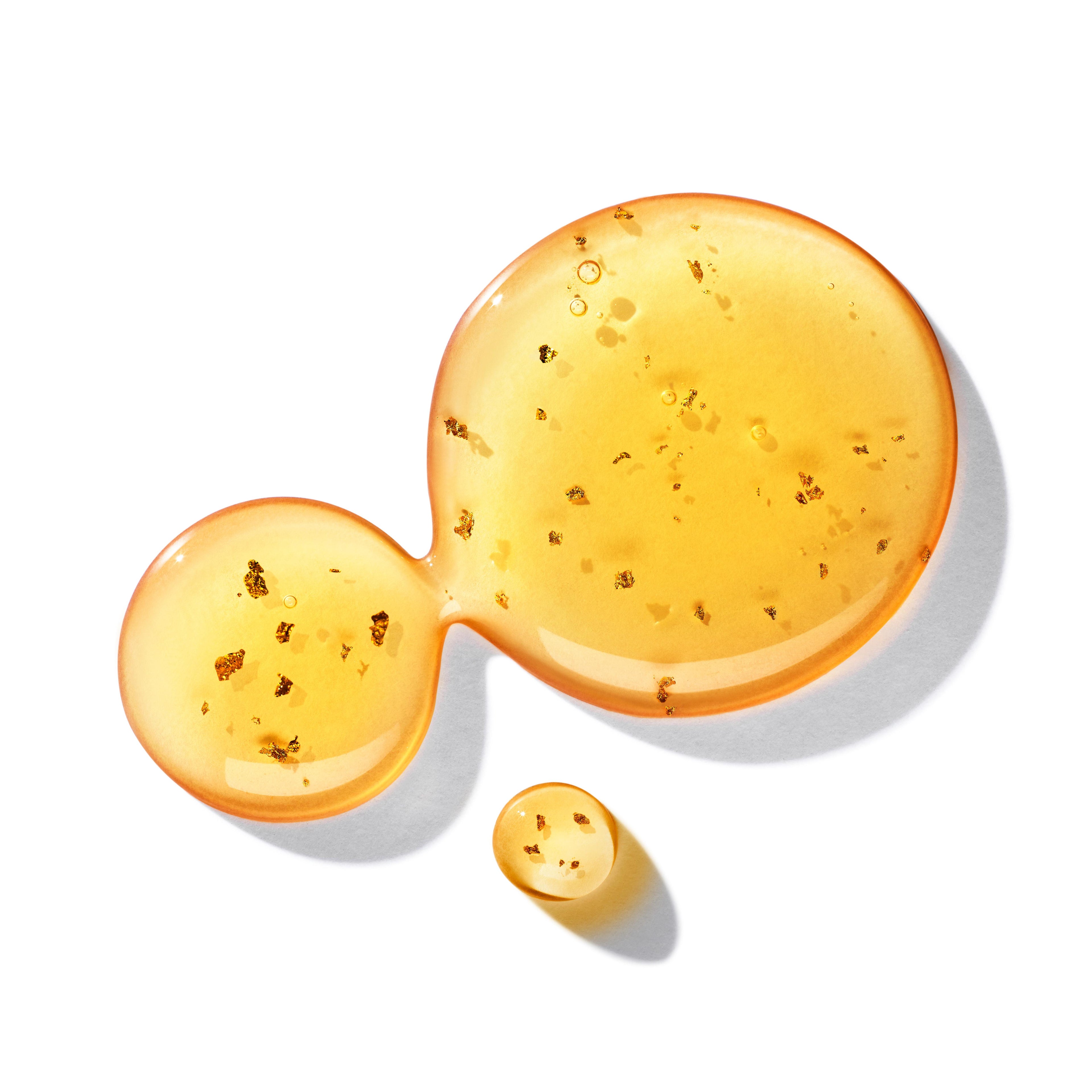 Three golden liquid droplets, enhanced with 23.5-carat golden flakes, shimmer on a white background. The largest droplet seamlessly connects to a medium one, followed by a smaller droplet below, capturing the luxurious essence of the Molton Brown Cyprus Mesmerising Oudh Accord & Gold Fine Liquid Hand Wash 300ml.