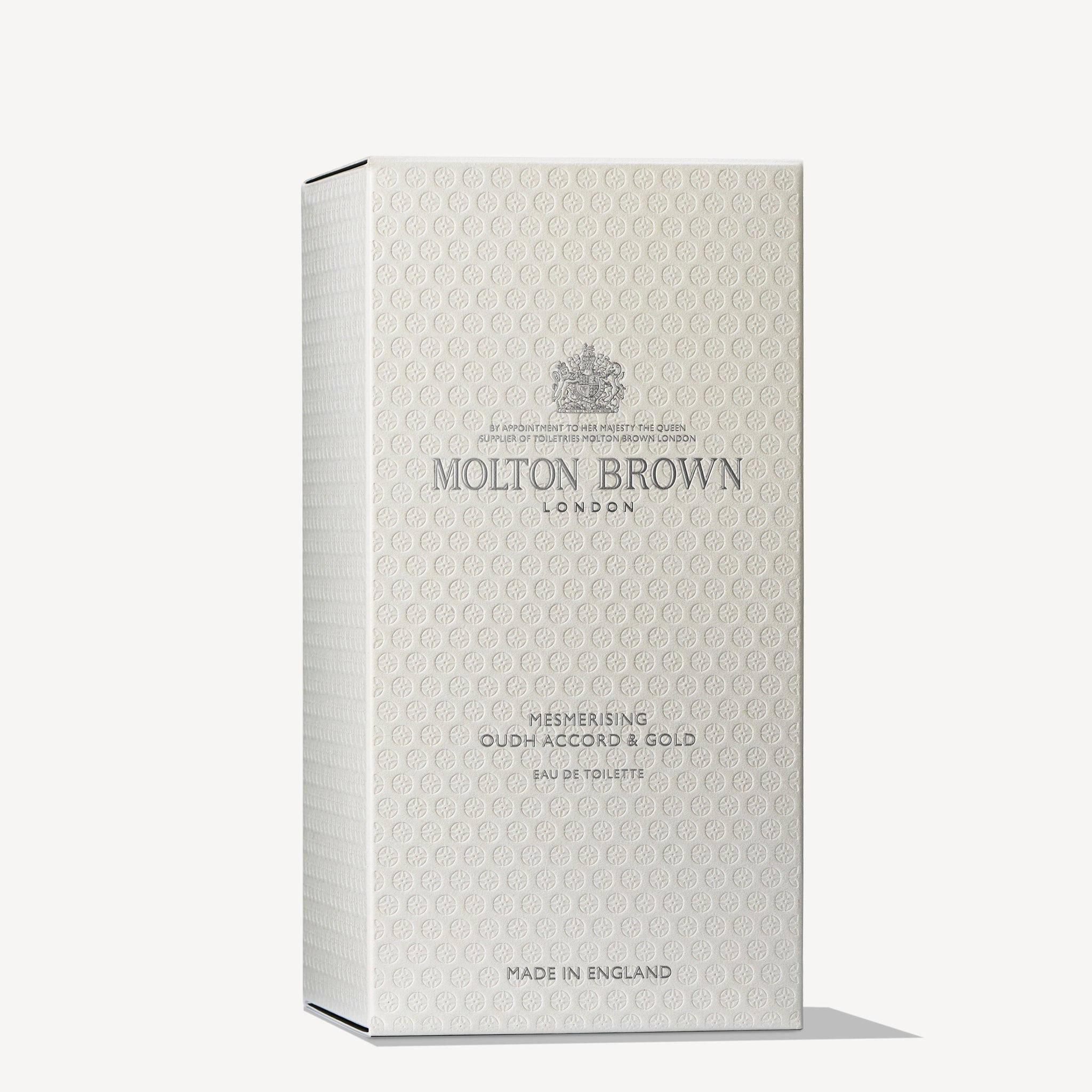 The product is presented in a chic beige rectangular box adorned with intricate patterns, featuring the MoltonBrown Cyprus logo alongside "Mesmerising Oudh Accord & Gold Eau de Toilette 100ml," with an underlying essence of black tea. "Made in England" is elegantly inscribed at the bottom.