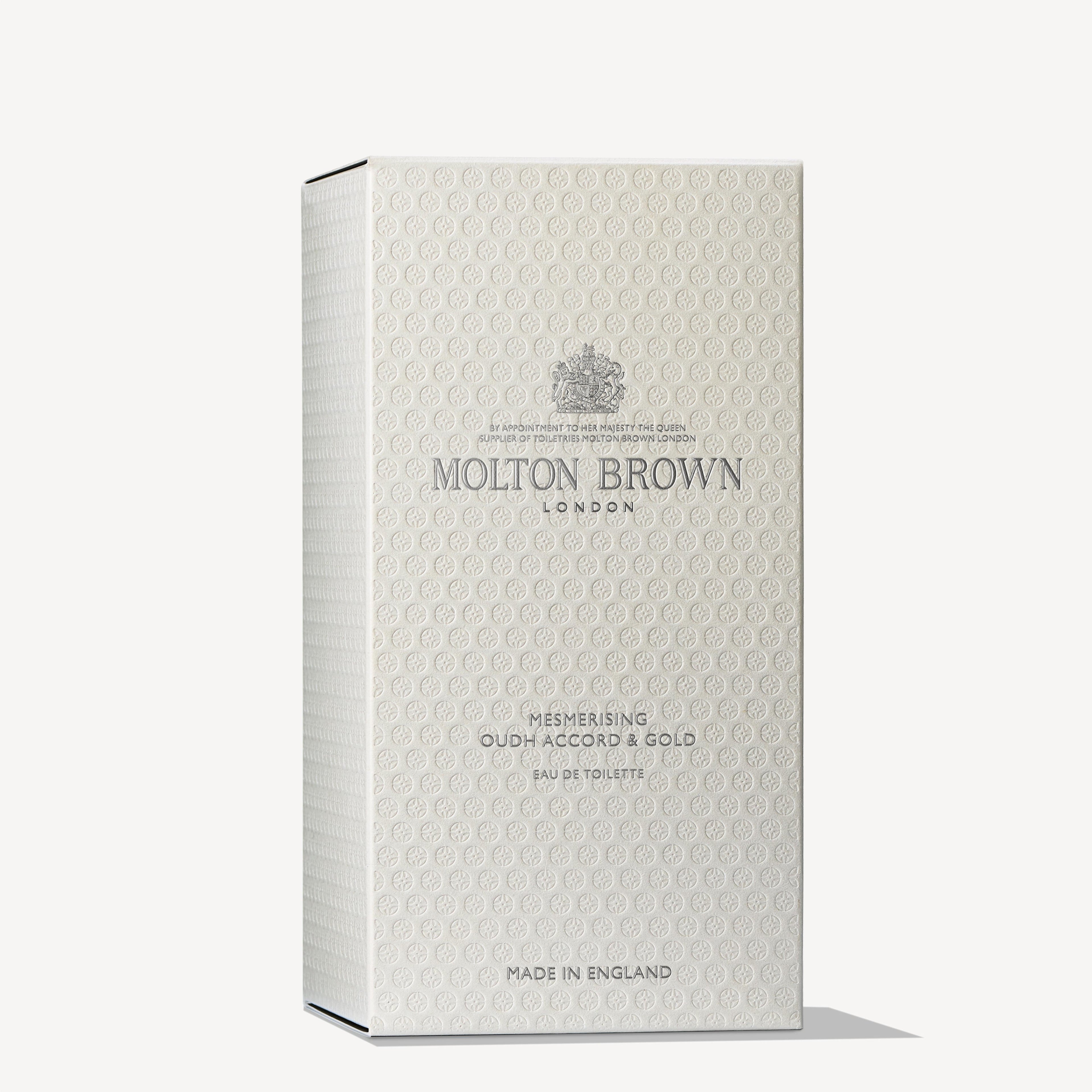 The product is presented in a chic beige rectangular box adorned with intricate patterns, featuring the MoltonBrown Cyprus logo alongside "Mesmerising Oudh Accord & Gold Eau de Toilette 100ml," with an underlying essence of black tea. "Made in England" is elegantly inscribed at the bottom.
