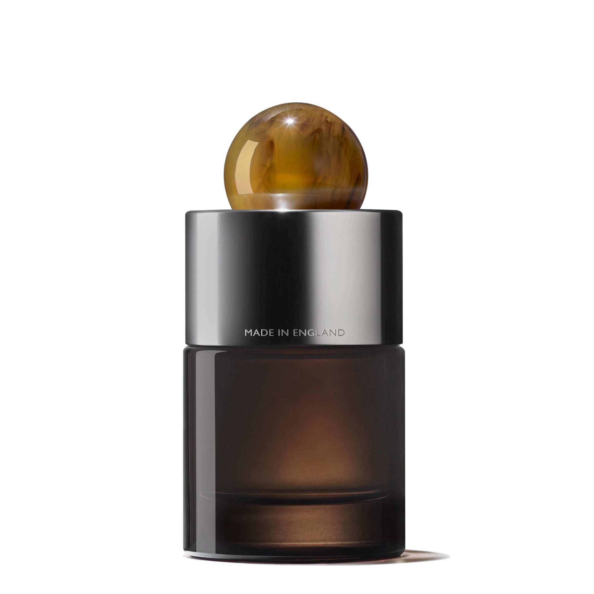 Introducing the sleek Tobacco Absolute Eau de Parfum by MoltonBrown Cyprus: a distinguished perfume bottle featuring a dark glass body and a silver cap, adorned with a spherical stone-like design. Inscribed with "Made in England," this elegant bottle houses an alluring woody fragrance infused with hints of smoky tobacco, embodying modern sophistication.