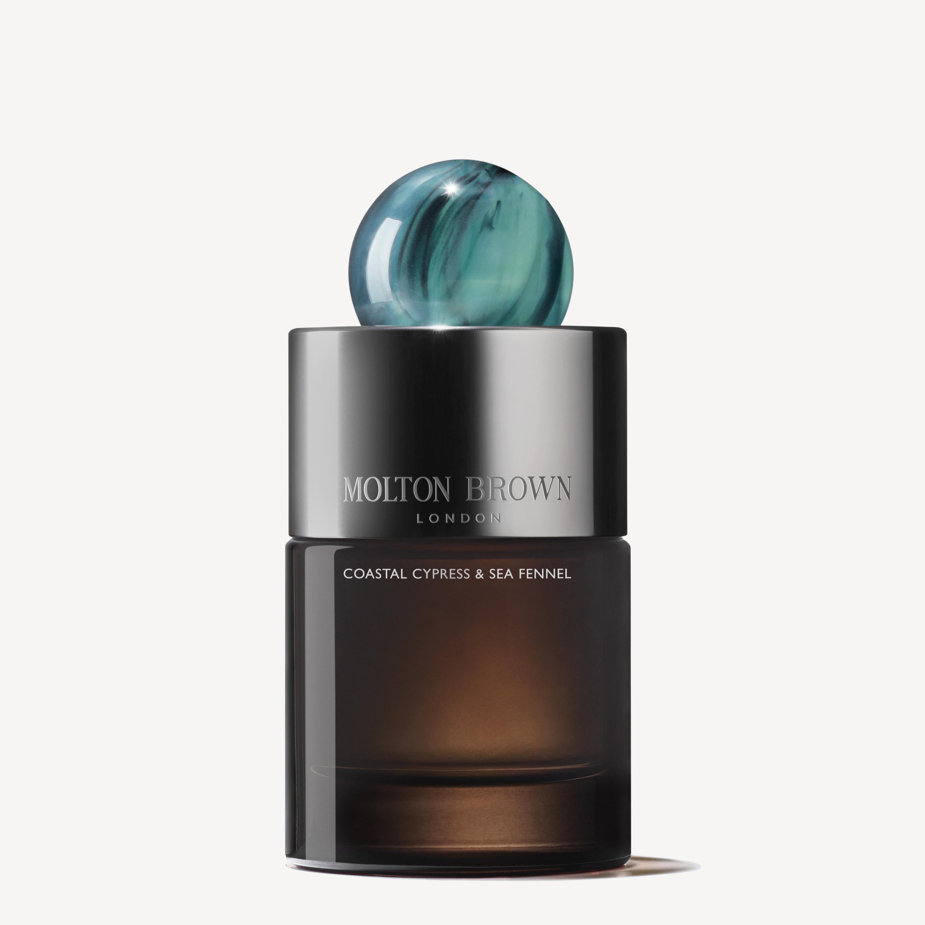 A cylindrical bottle of MoltonBrown Cyprus Coastal Cypress & Sea Fennel Eau de Parfum features a metallic cap and a blue marble-like top. The ocean-inspired fragrance is captured on the label, and the bottle showcases a gradient from dark to light brown.