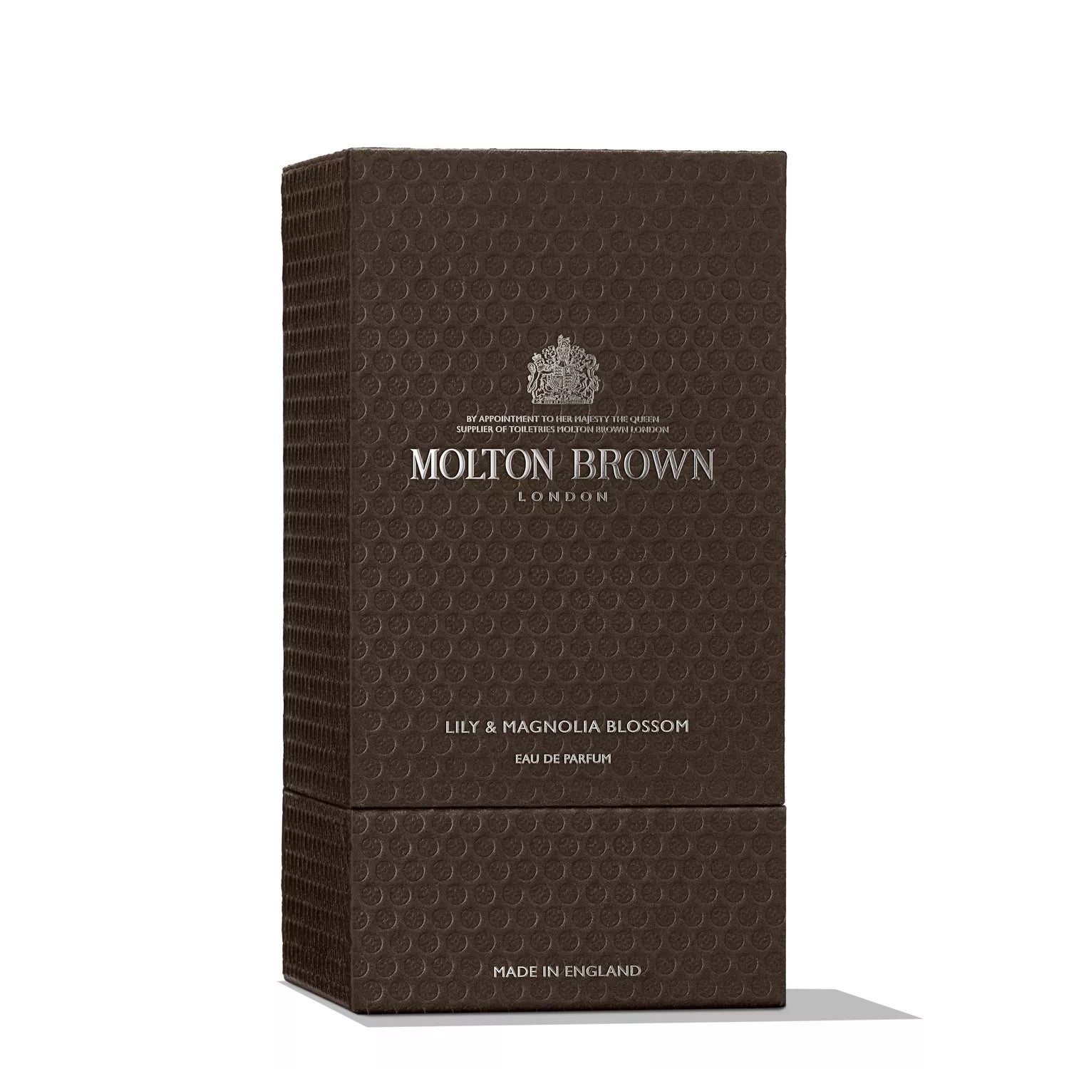 A brown textured box featuring Molton Brown Cyprus and Lily & Magnolia Blossom Eau de Parfum 100ml elegantly written in silver. This exquisite floral scent is Made in England, with an embossed pattern and a top logo.