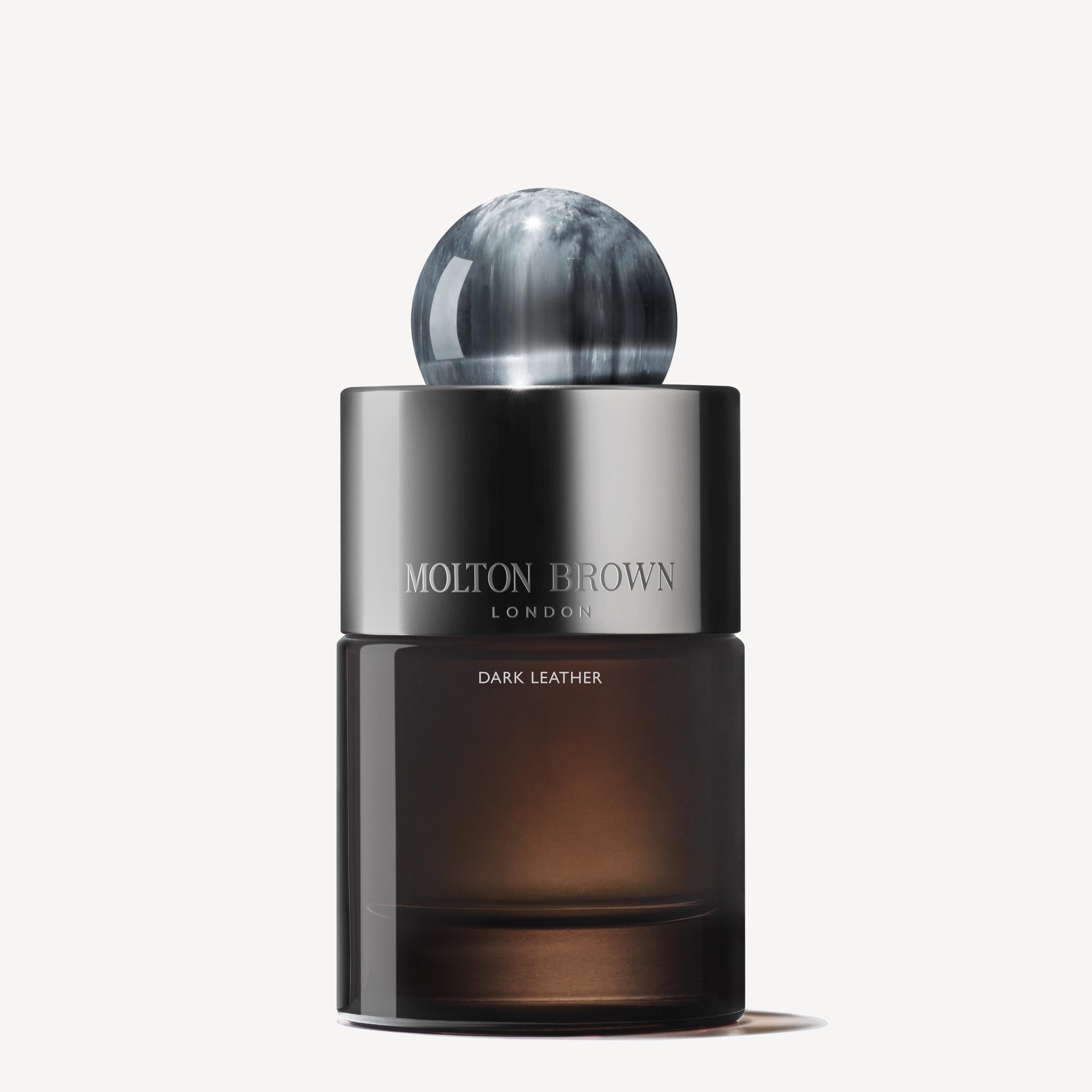The Dark Leather Eau de Parfum 100ml from MoltonBrown Cyprus features a sleek, dark design with a reflective sphere cap and a gradient glass base. It is infused with smoky leather notes, while the brand name is elegantly printed in white on a silver band at the top.