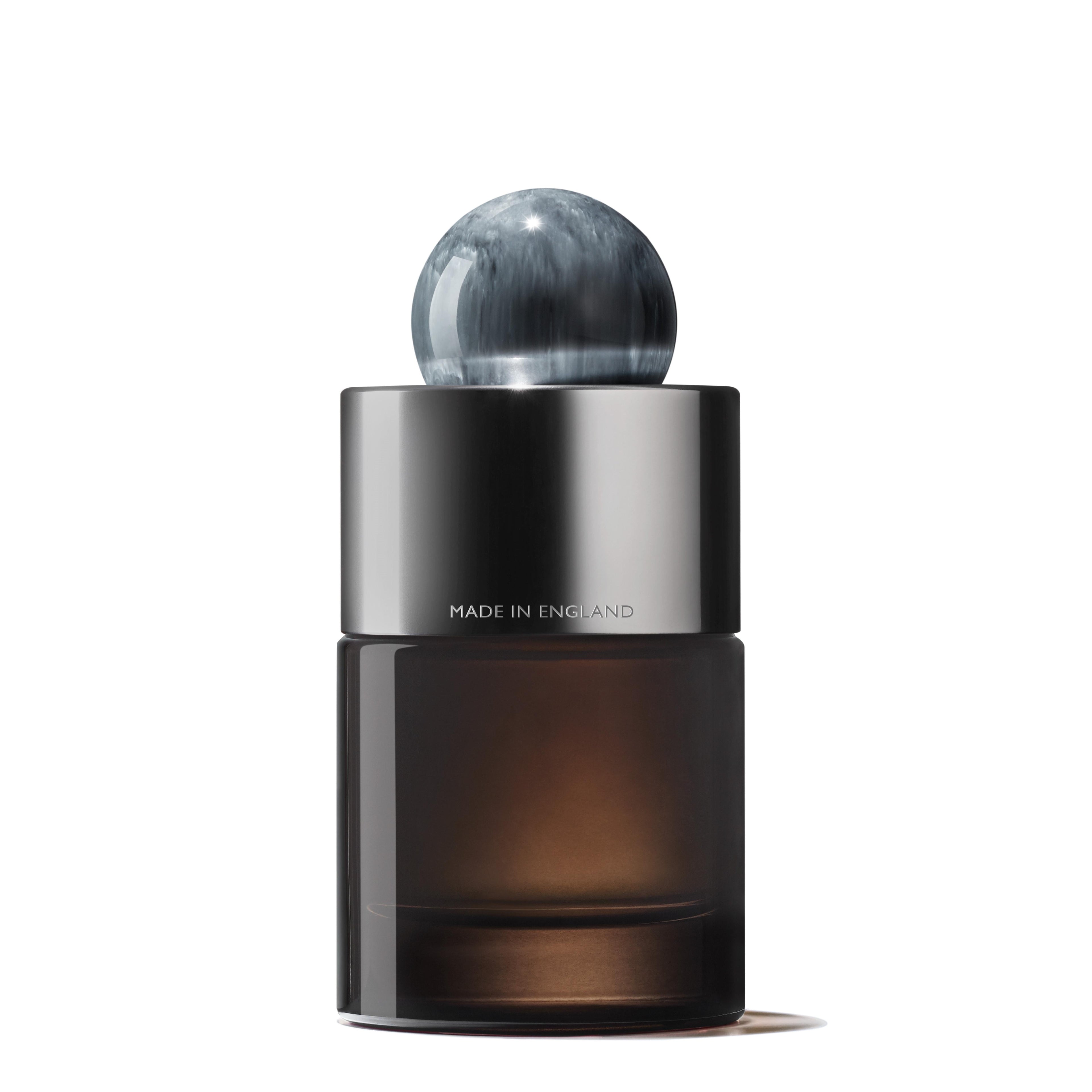 A sleek, minimalist bottle from MoltonBrown Cyprus for the Dark Leather Eau de Parfum, featuring a dark, translucent base and a shiny silver band around the neck engraved with "Made in England." The woody fragrance is complemented by a spherical, marble-like gray cap.