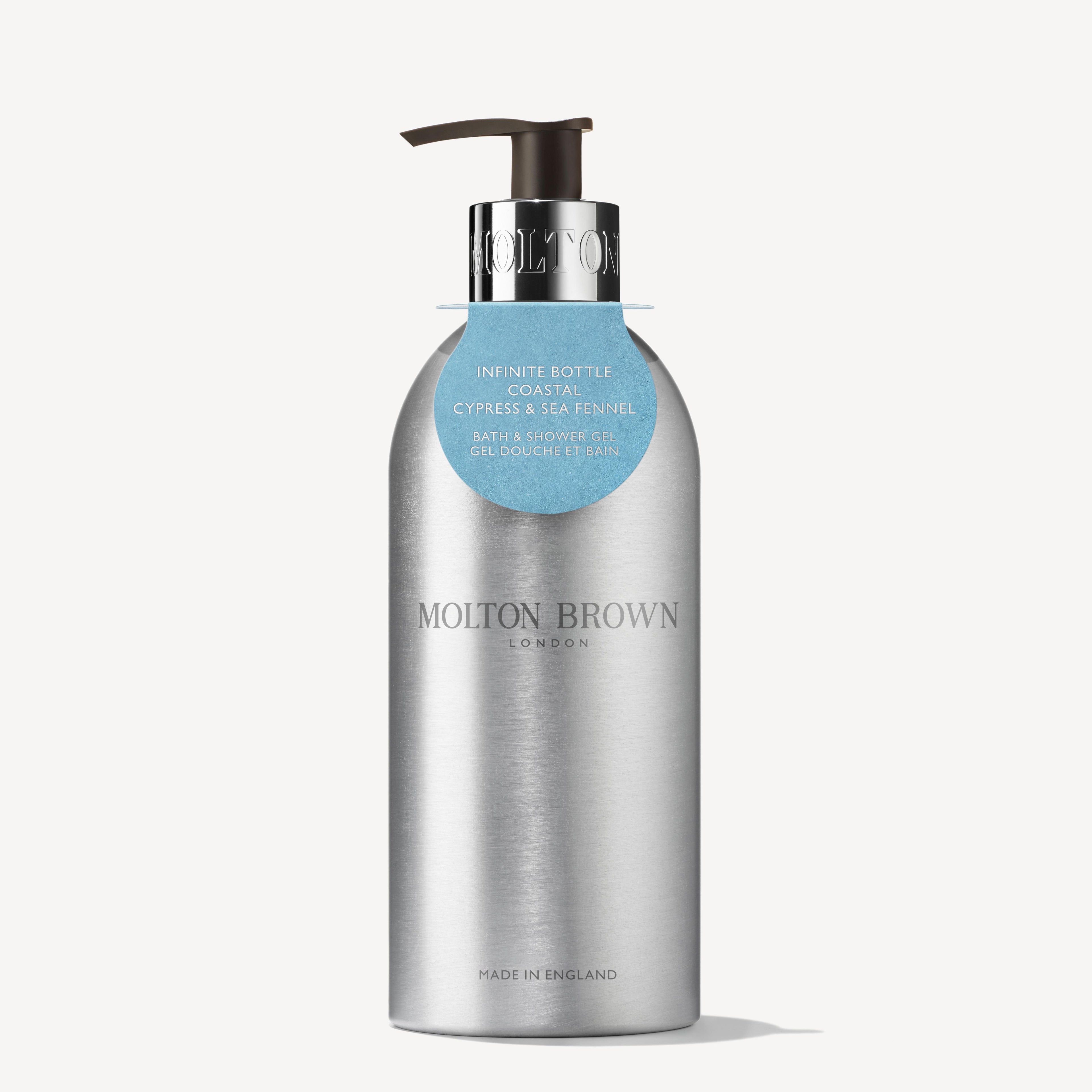 A 400ml silver recycled aluminum MoltonBrown Cyprus bottle of bath and shower gel, featuring a black pump and adorned with a blue tag at the neck. The label displays "Coastal Cypress & Sea Fennel," and "Made in England" is printed at the bottom, making it an ideal choice for a sustainable bathing routine.