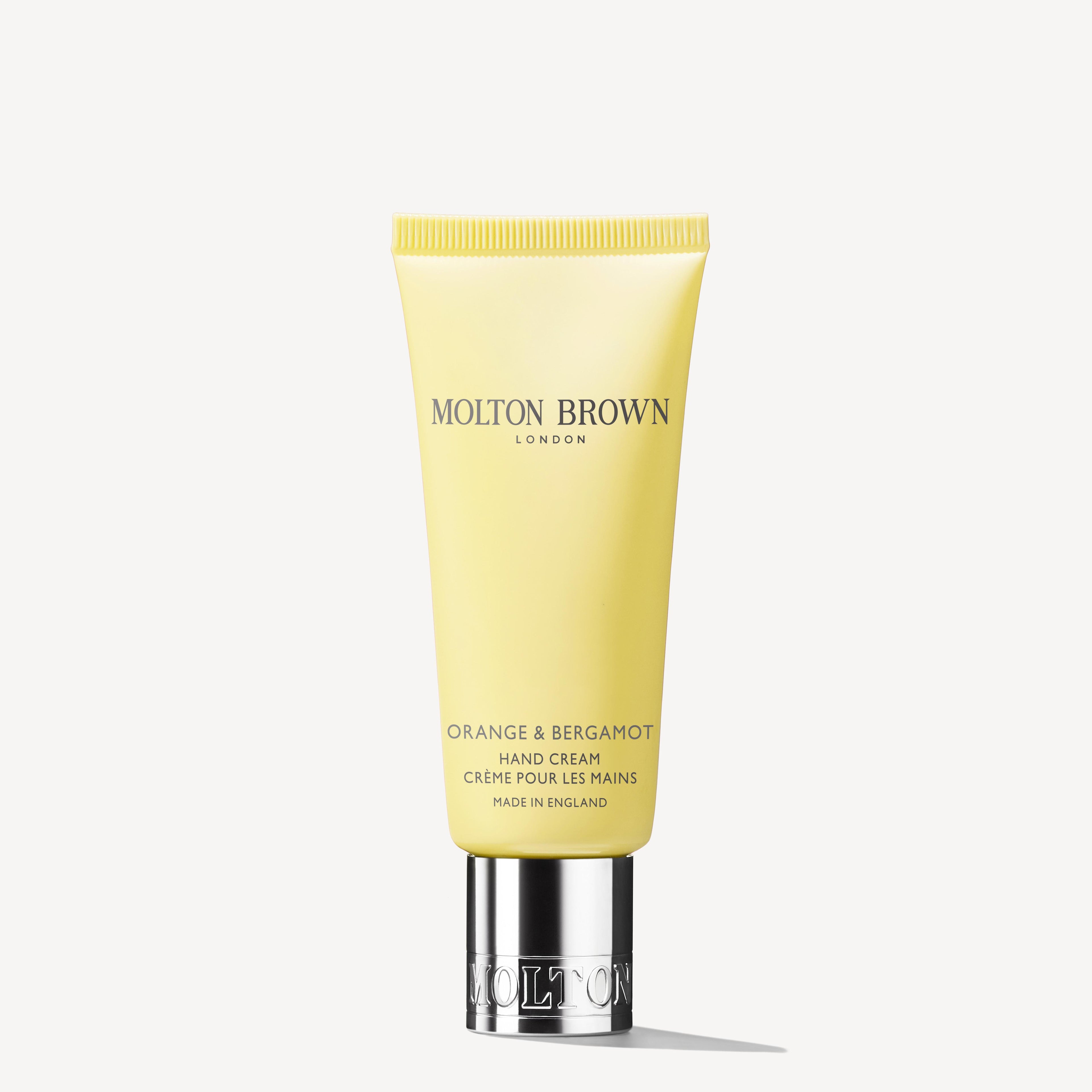 An Orange & Bergamot Hand Cream 40ml by MoltonBrown Cyprus, in a yellow tube with a silver cap, stands upright. The label features text and a crest logo that highlights hints of mandarin and neroli against a plain white background.
