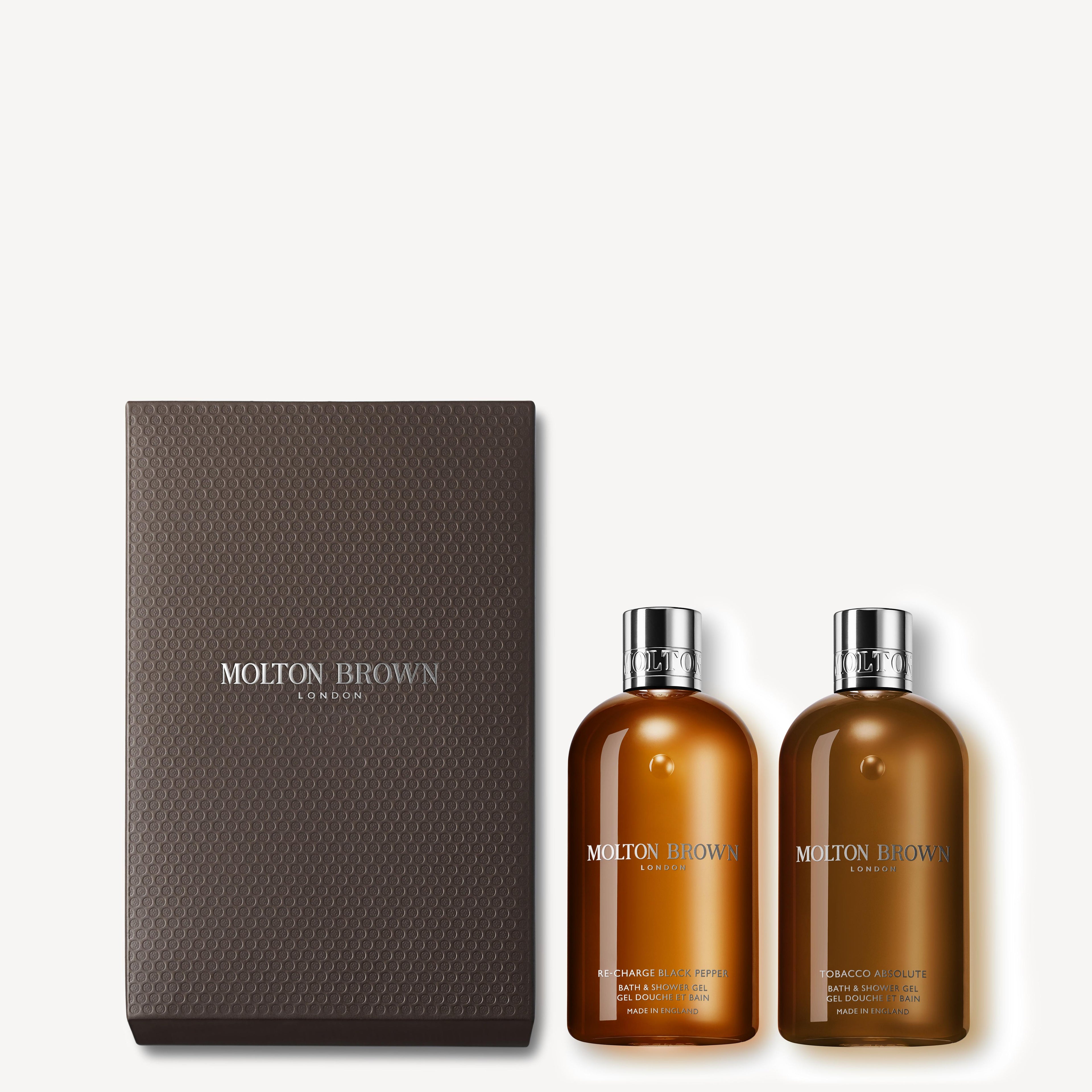 A MoltonBrown Cyprus Re-charge Black Pepper & Tobacco Absolute Shower Gel Gift Set that includes two sophisticated brown bottles of body wash, presented in a textured black box embellished with the Molton Brown logo.