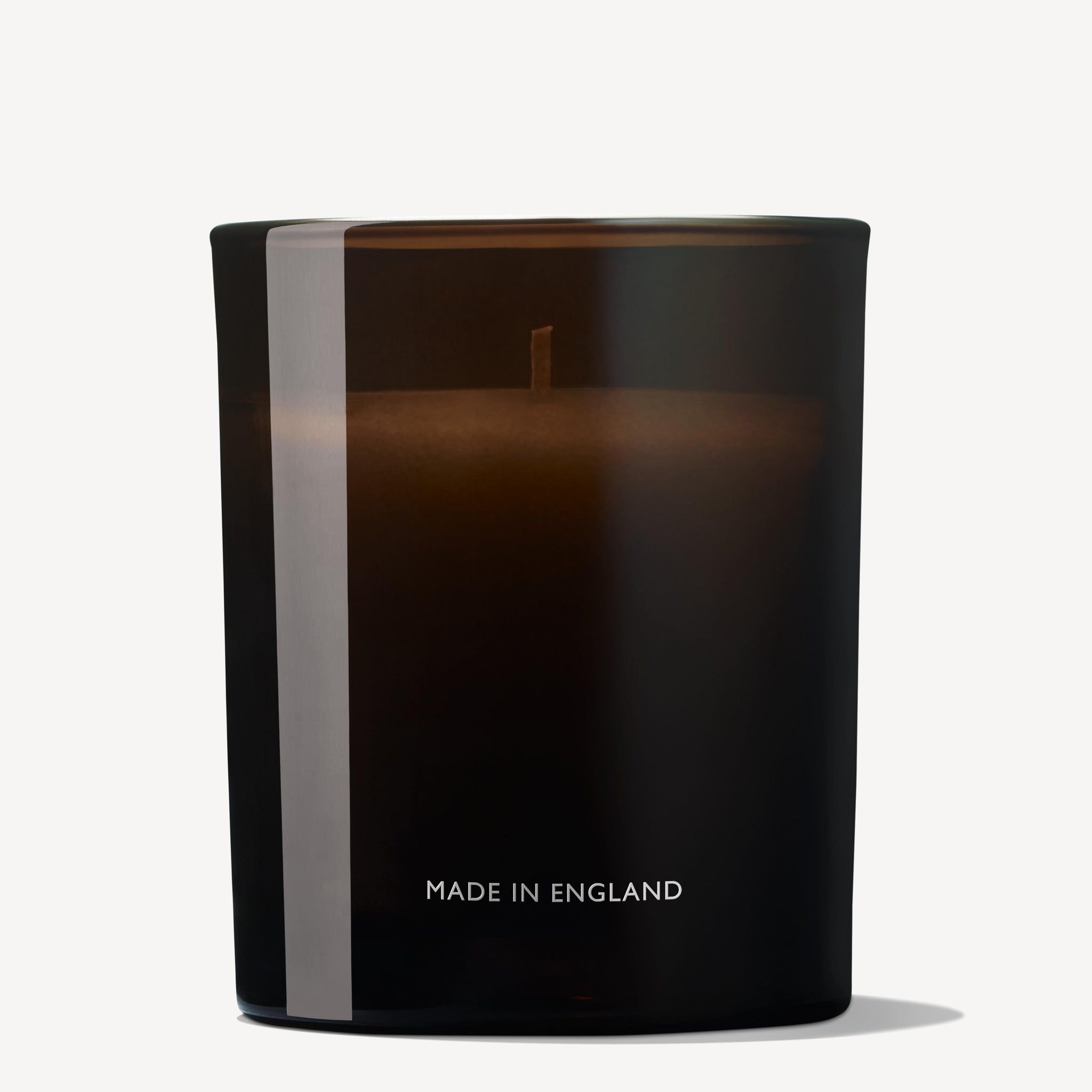 A dark brown glass single-wick candle holder labeled "Made in England" at the base, containing the Orange & Bergamot Signature Candle 190g by Molton Brown Cyprus. The visible wick is set to infuse your space with a delicate orange mandarin fragrance, all against a gentle, off-white background.