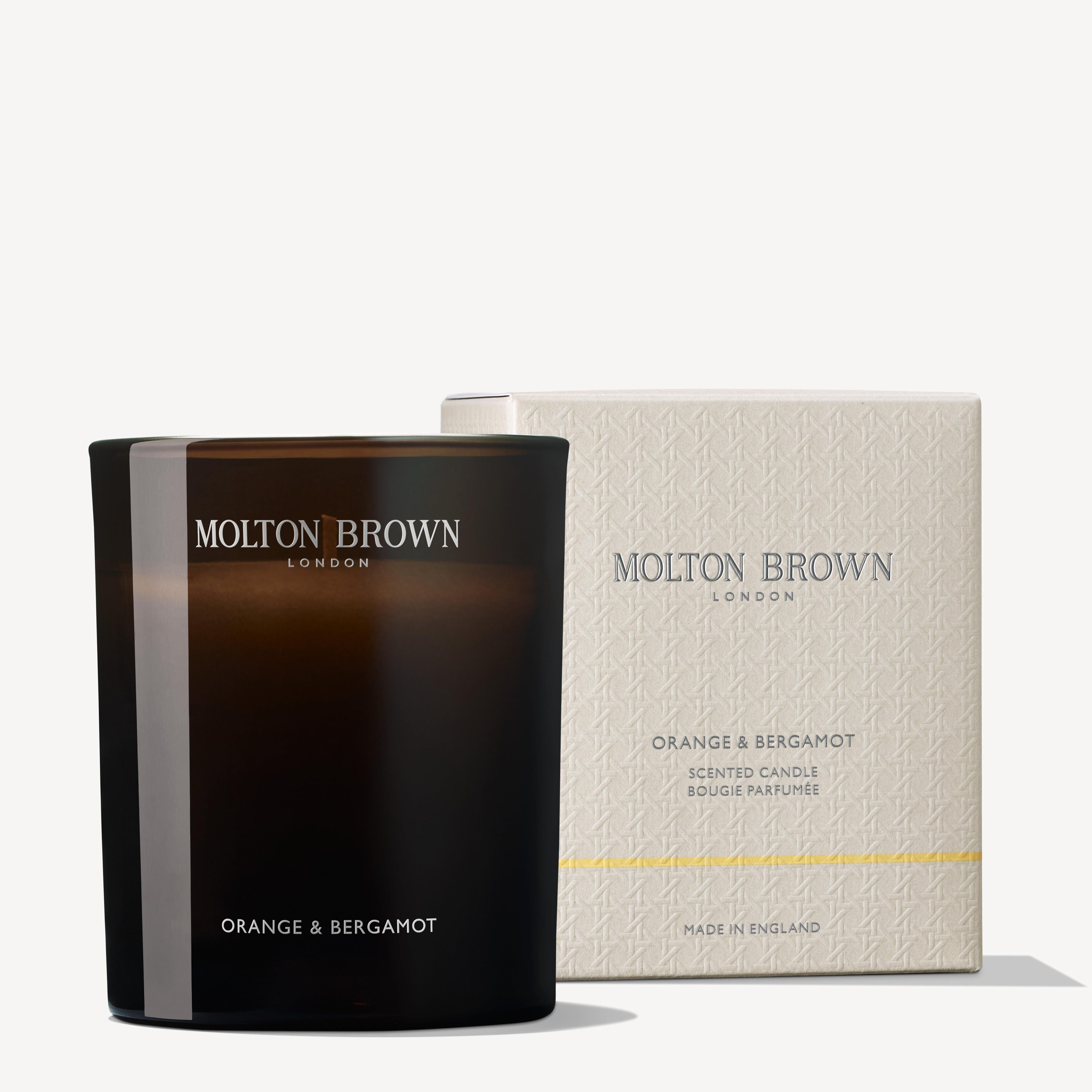 A Molton Brown Cyprus Orange & Bergamot Signature Candle 190g, infused with a refreshing aroma, rests in a dark glass jar beside its elegant cream-colored box. The packaging text highlights the Molton Brown Cyprus brand and the distinctive scent of this single wick candle.