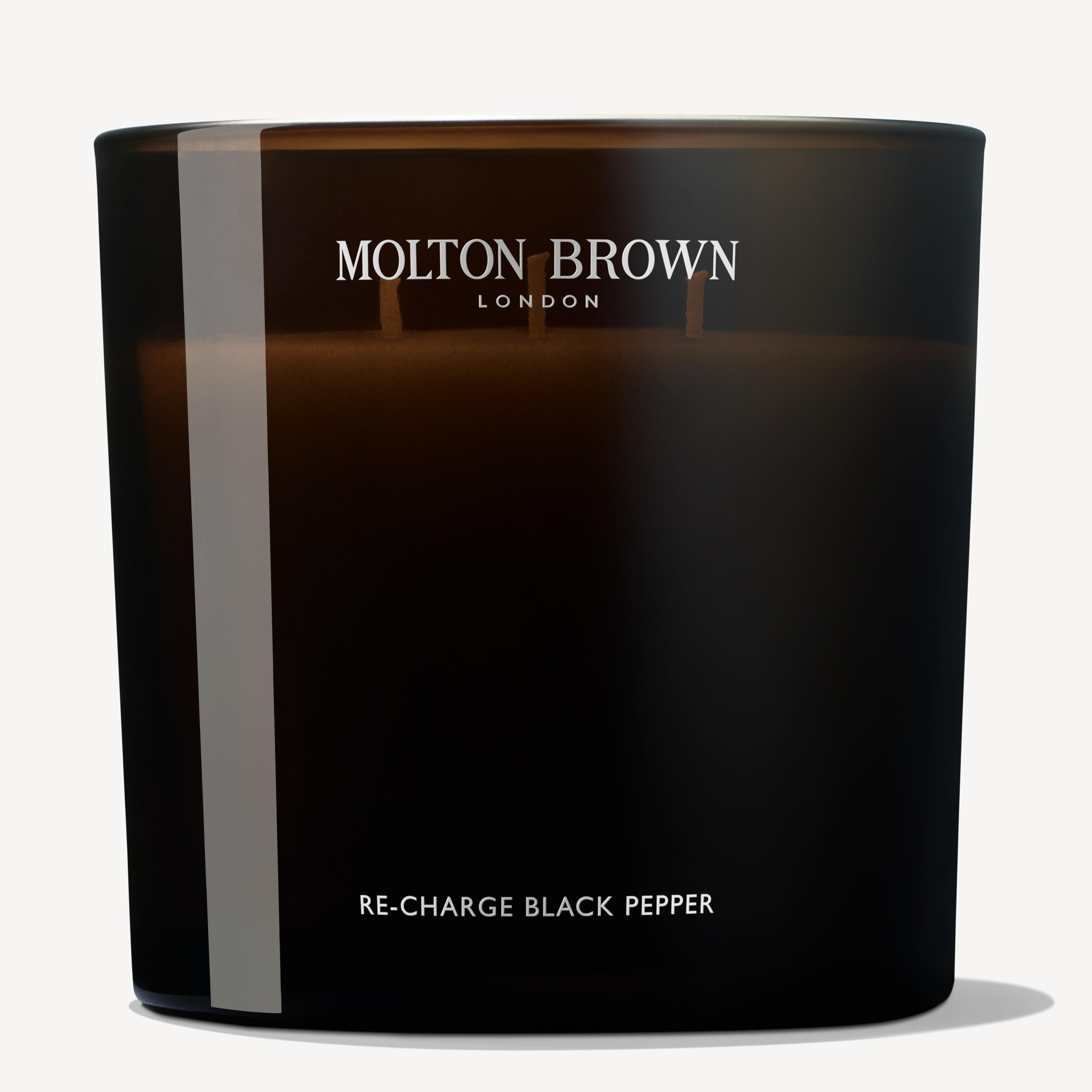 A Re-charge Black Pepper Luxury Candle 600g from MoltonBrown Cyprus, crafted from recycled materials and featuring two wicks, releases the invigorating scent of Madagascan black pepper. The black candle is displayed on a plain, light background.