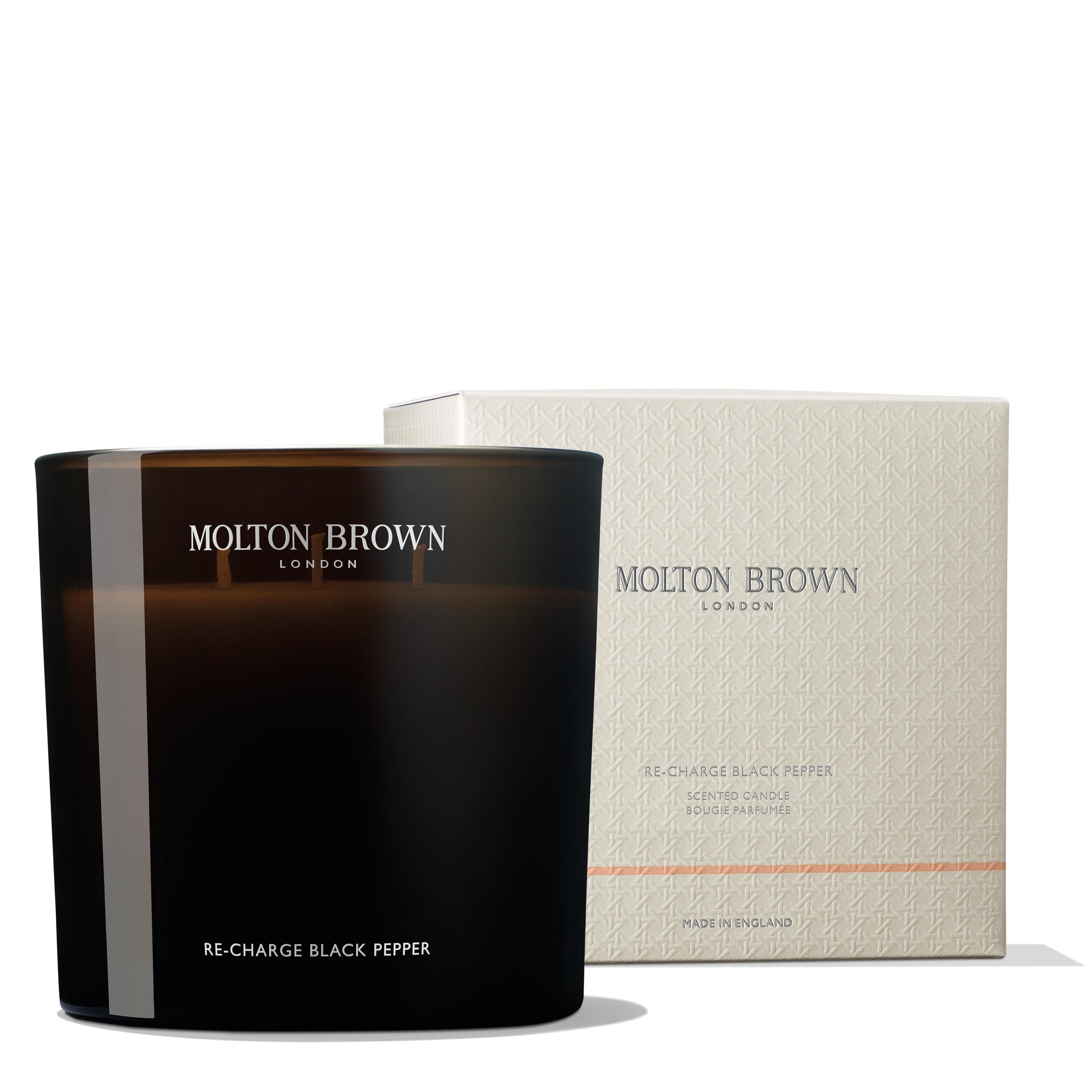 A MoltonBrown Cyprus Re-charge Black Pepper Luxury Candle 600g, infused with Madagascan black pepper, is placed next to its matching box. The candle, crafted in a sleek black container, complements the light-colored box made from recycled materials and featuring a subtle pattern and text.