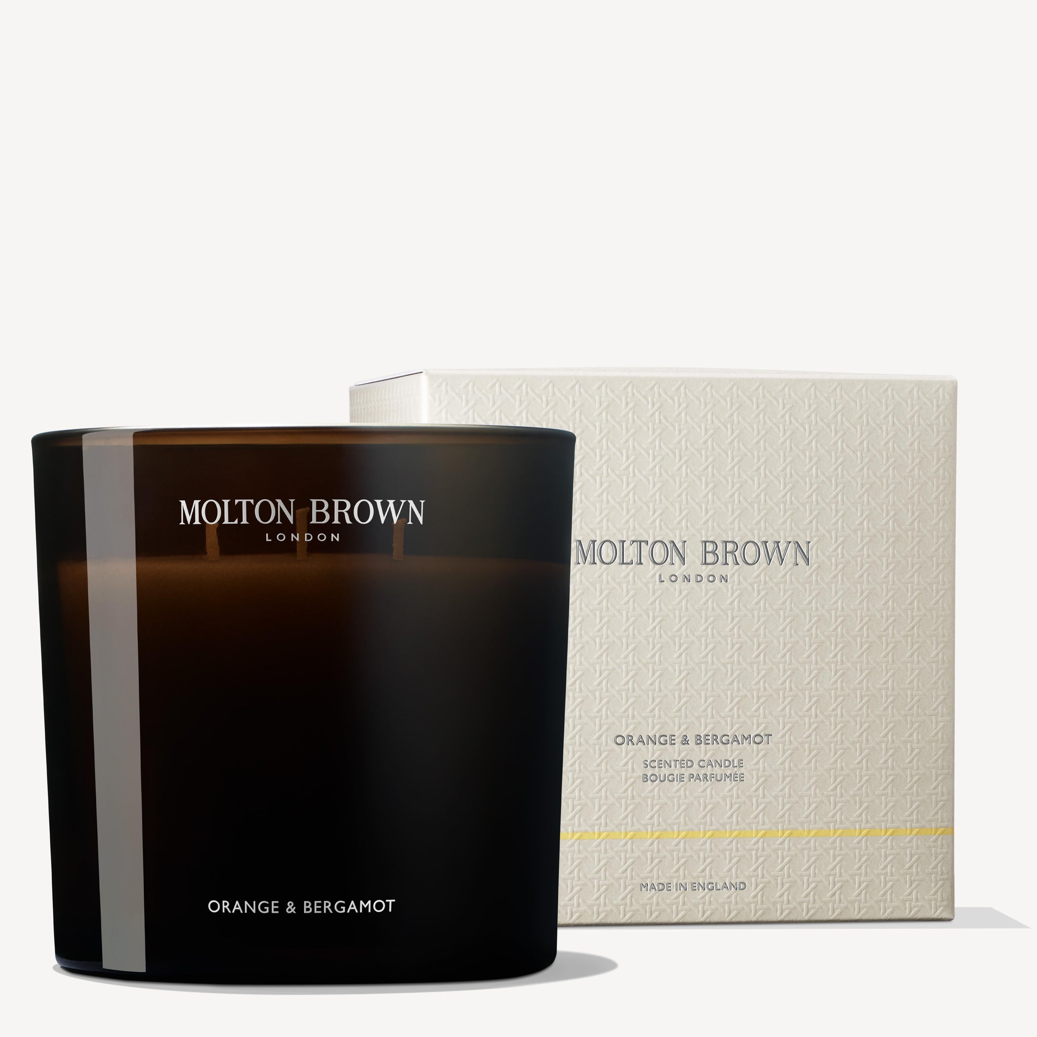 The MoltonBrown Cyprus Orange & Bergamot Luxury Candle 600g, presented in a dark glass holder and made from recycled materials, is elegantly displayed in front of its beige box packaging, which prominently features the brand's logo.