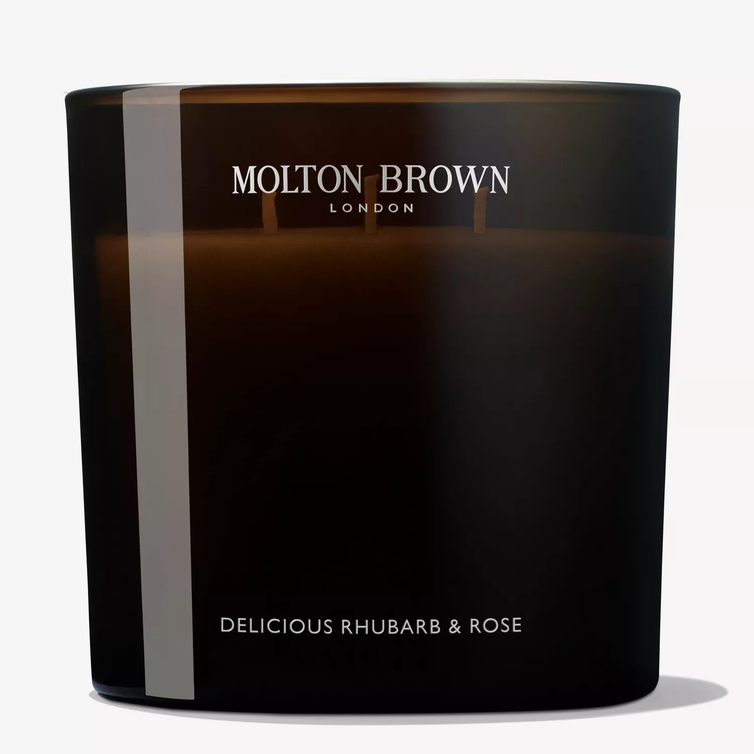 A Delicious Rhubarb & Rose Luxury Candle by MoltonBrown Cyprus, encased in a dark glass container, offers an unlit floral-fruity essence with notes of grapefruit and features the brand name elegantly displayed at the top.