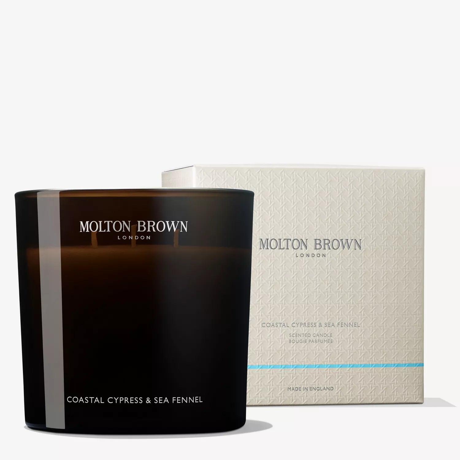 The MoltonBrown Cyprus Coastal Cypress & Sea Fennel Luxury Candle 600g is presented in a refined black glass container, offering the essence of salted cypress and marine notes. It sits gracefully next to its white packaging, which features the brand name and product information in elegant lettering.