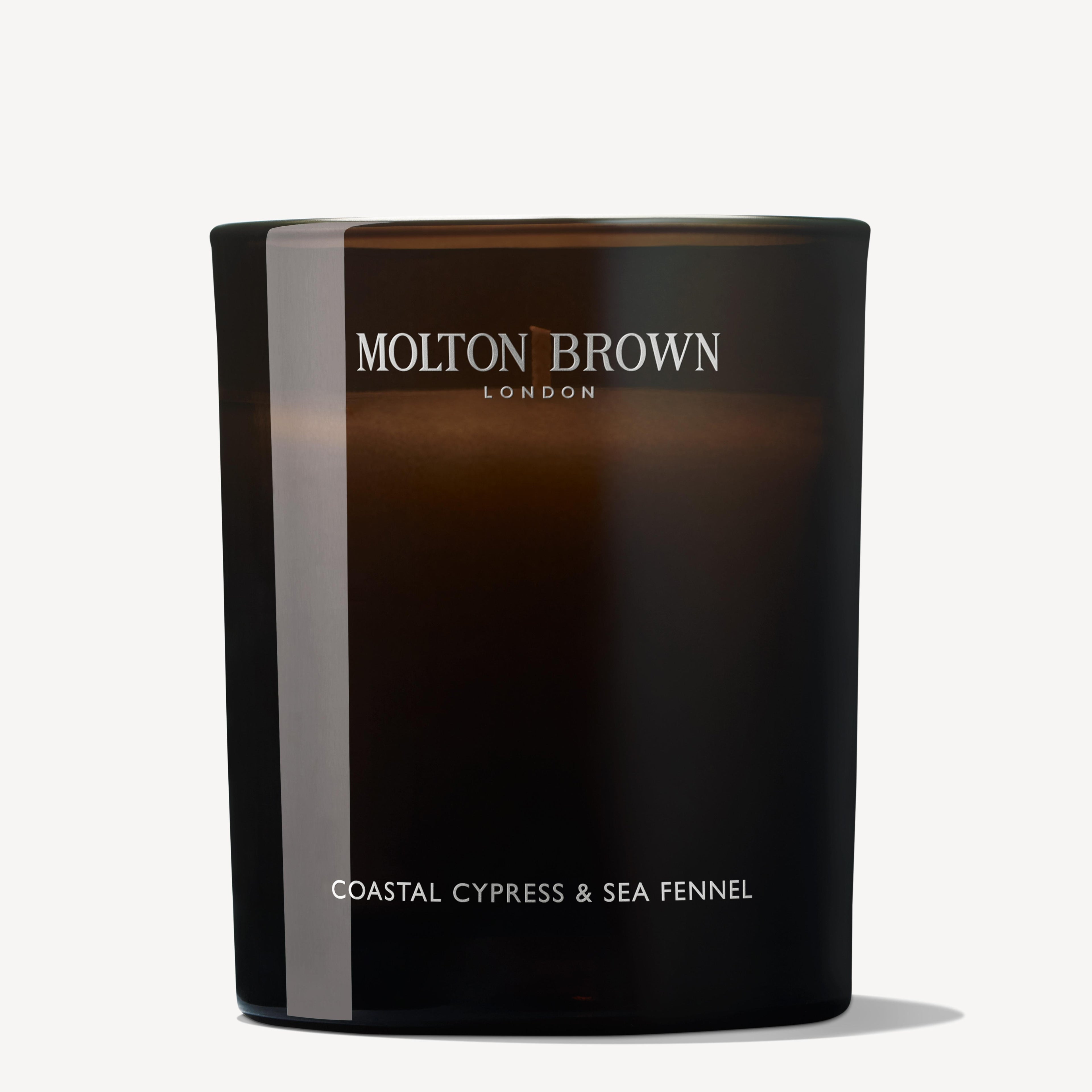 A Coastal Cypress & Sea Fennel Signature Candle 190g from MoltonBrown Cyprus, made of dark glass, showcases a sleek, minimalist design with a soft, reflective surface. It exudes enticing marine notes and prominently displays the brand name at the top.