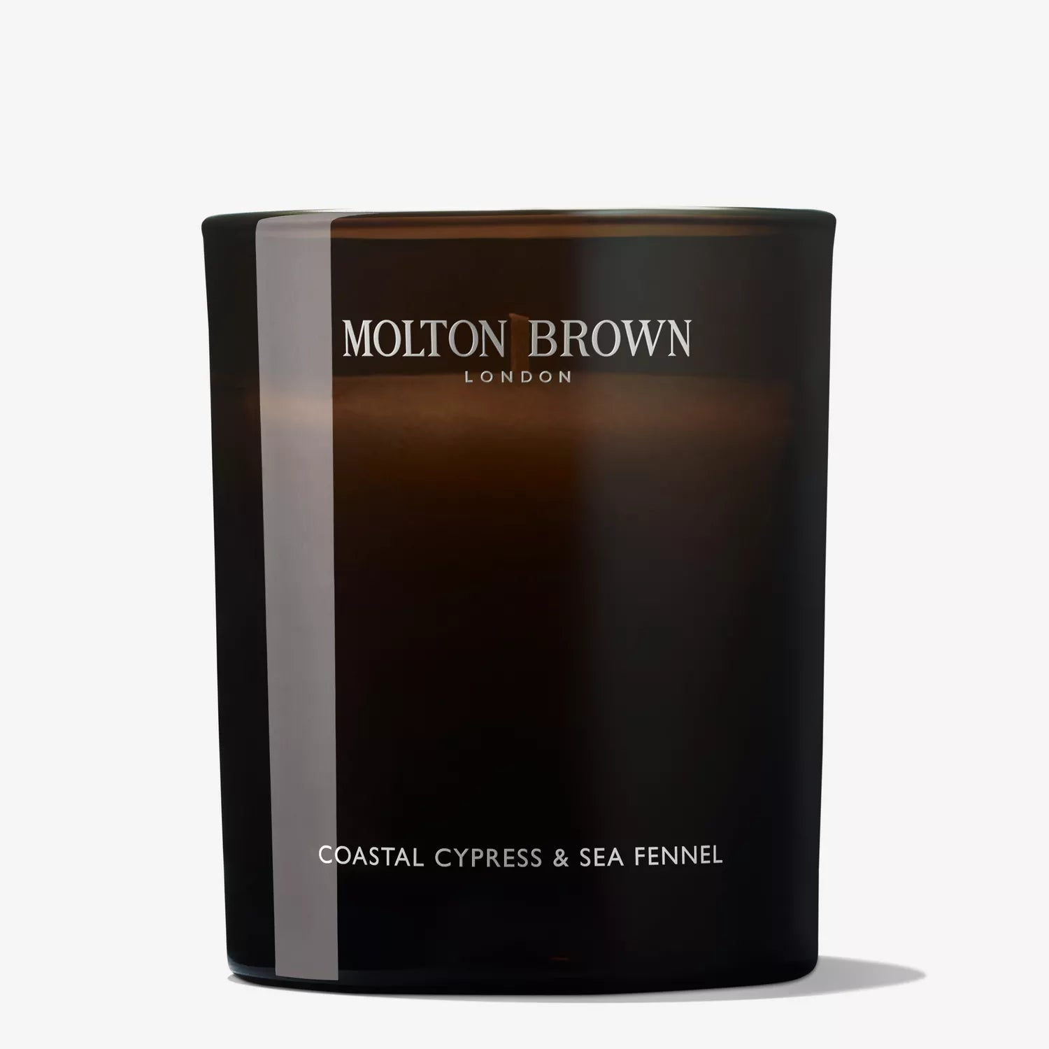 A Coastal Cypress & Sea Fennel Signature Candle 190g from MoltonBrown Cyprus, housed in a dark glass container, stands against a plain white background, exuding invigorating marine notes.