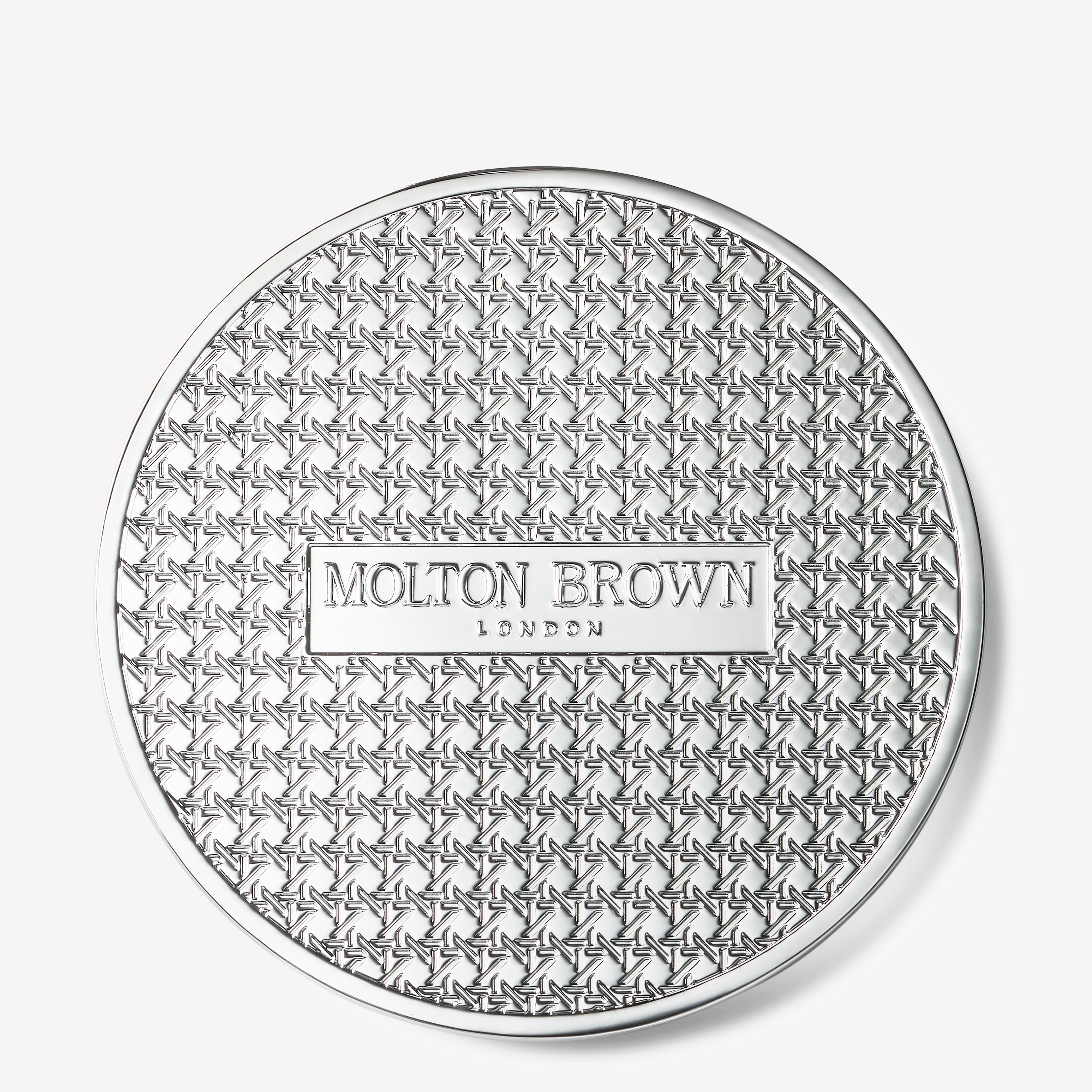 A circular lid made of silver metal, similar to chrome plating, showcases an elaborate star design with a raised rectangle at its center that bears the text "MoltonBrown Cyprus.