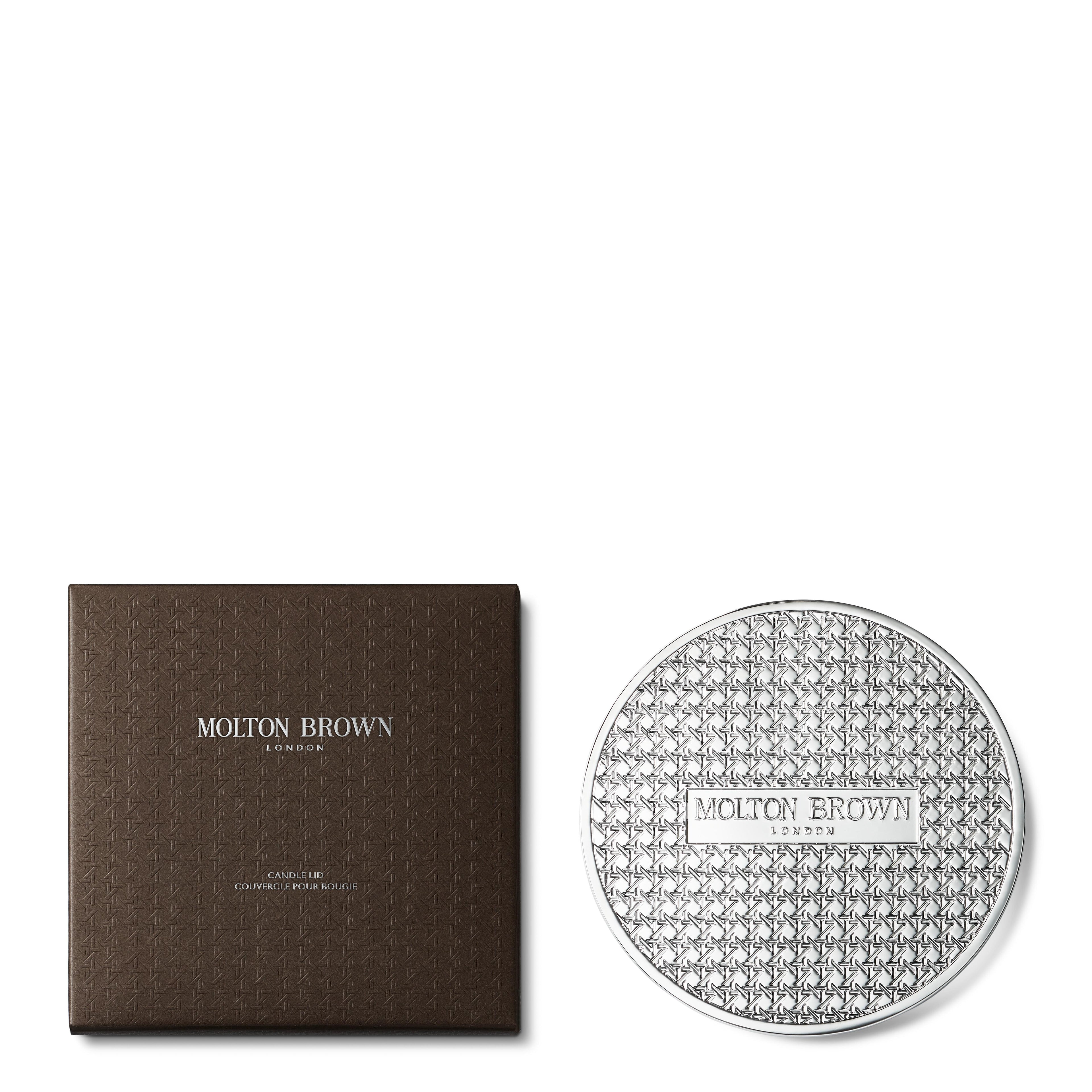 A MoltonBrown Cyprus Luxury Candle Lid weighing 154g is displayed next to a chrome-plated, silver-textured container, elegantly labeled on the right. The dark square packaging with its striking silver branding exudes sophistication, evoking a luxurious allure similar to that of scented candles.