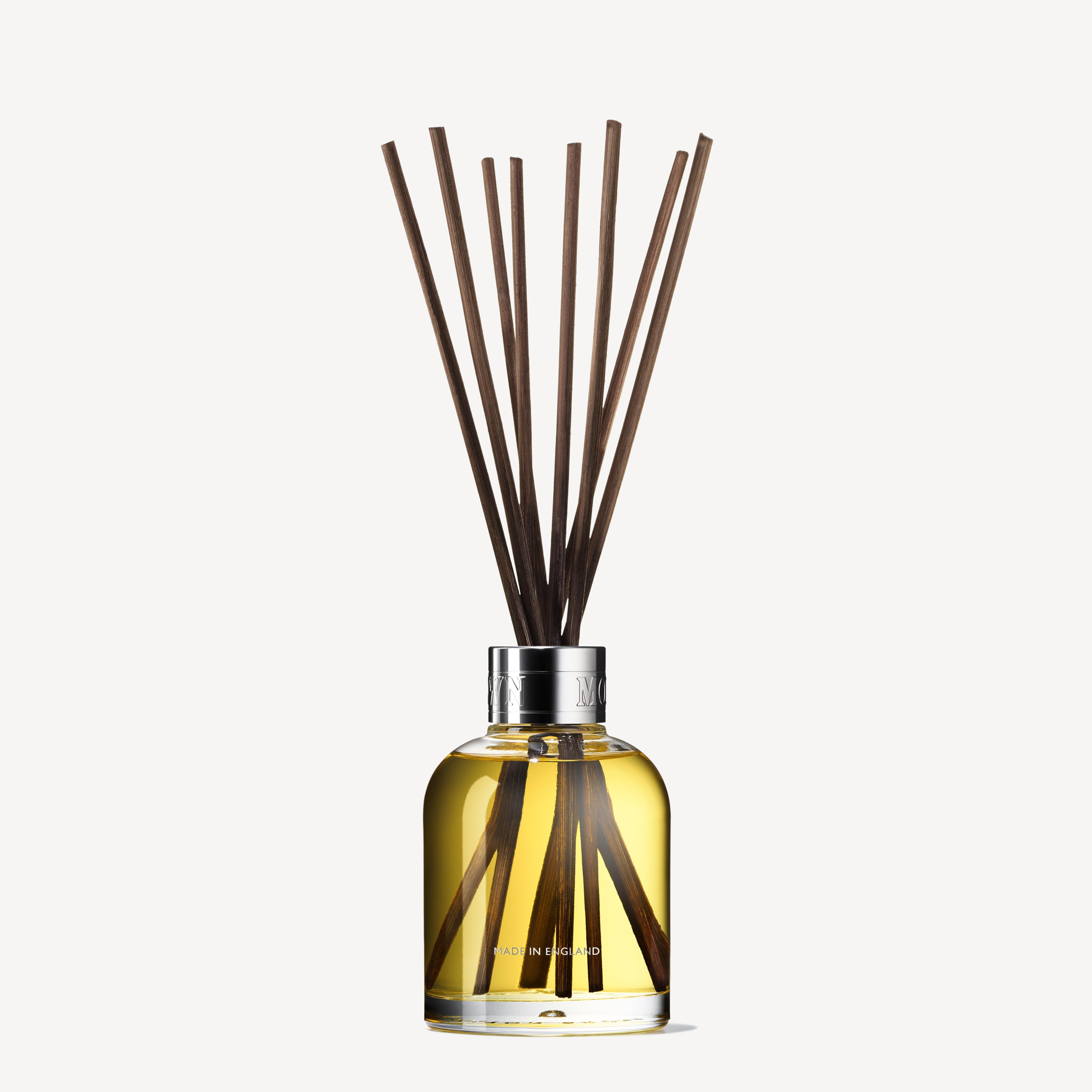 The Orange & Bergamot Aroma Reeds 150ml by MoltonBrown Cyprus elegantly stands as a reed diffuser, featuring a glass bottle filled with yellow liquid and several dark wooden reeds. The alluring scent of neroli blends with Sevillian orange notes wafting from its metallic-capped vessel, set against a light-colored background.