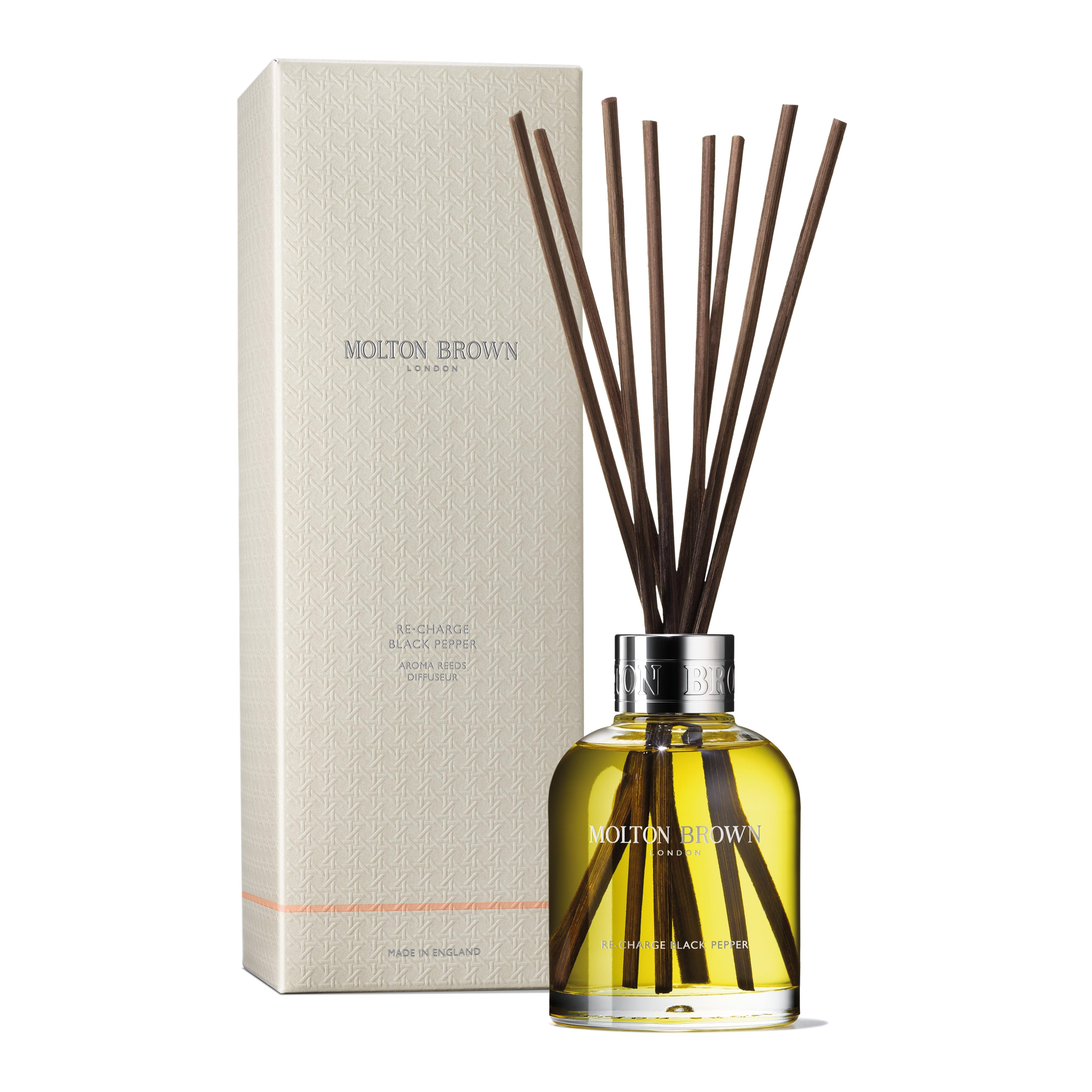 A MoltonBrown Cyprus Re-charge Black Pepper Aroma Reeds with woody-citrus notes and wooden reeds stands elegantly in a glass bottle filled with yellow liquid, set before a cream-colored branded box.