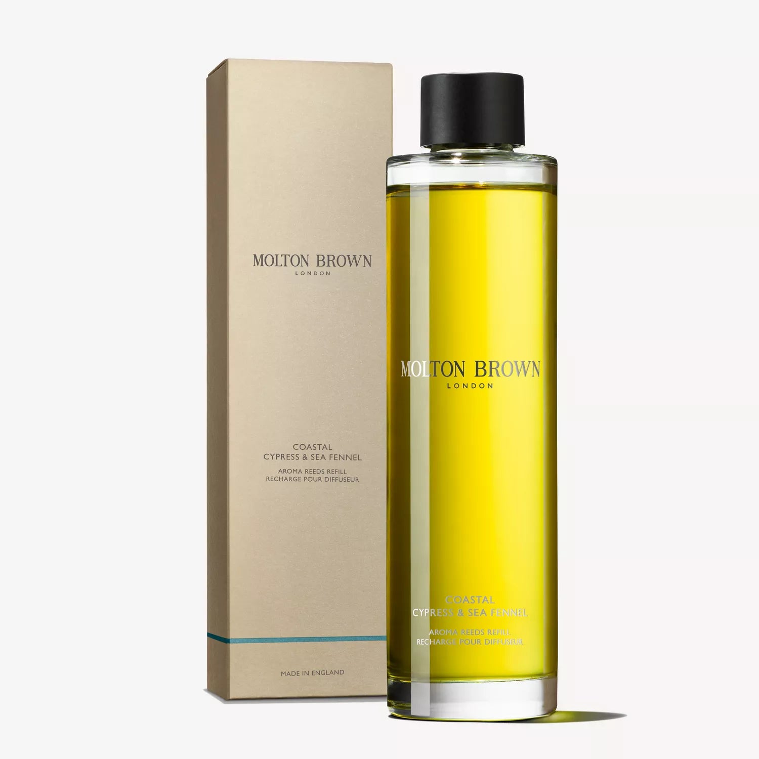 A Molton Brown Cyprus Coastal Cypress & Sea Fennel Aroma Reeds Refill, 150ml bottle with marine notes and a black cap, containing yellow liquid, elegantly displays its brand and name on both the cylinder and the beige box beside it.