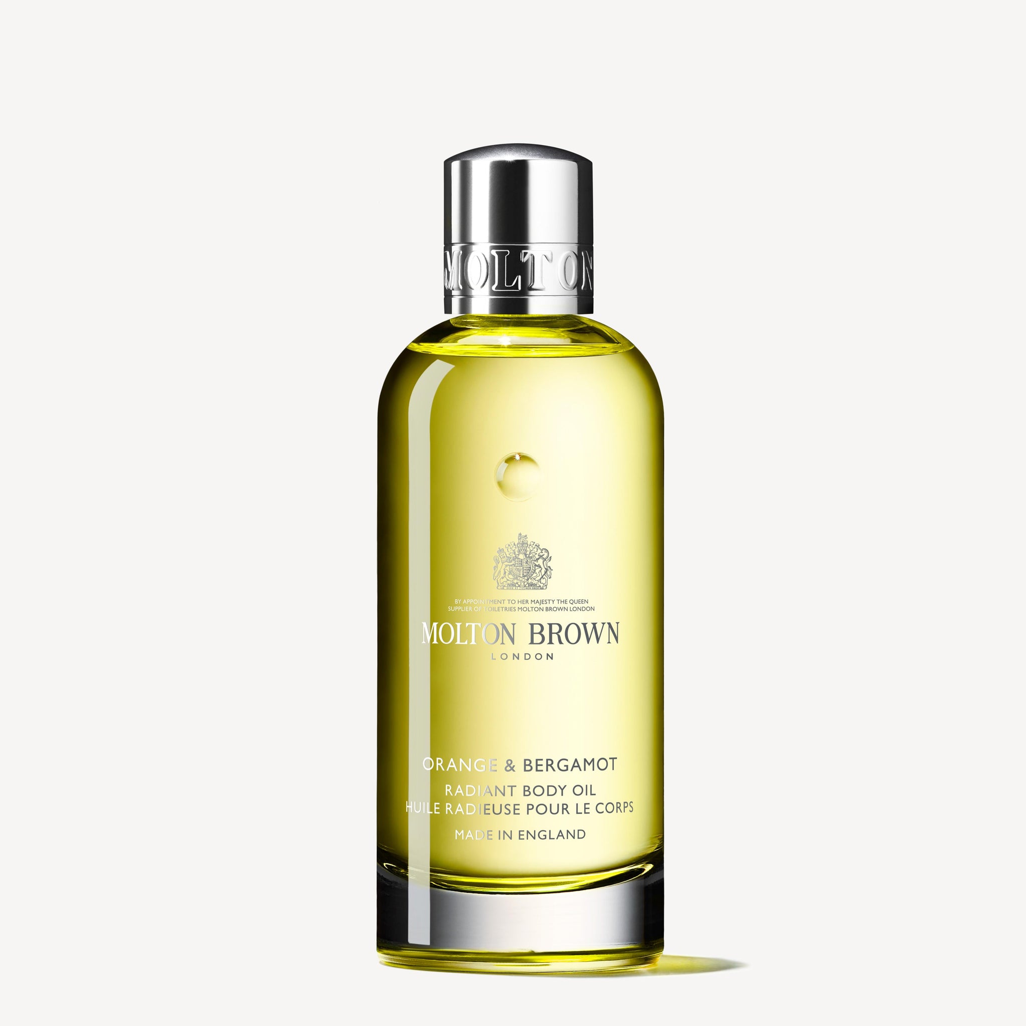 A clear bottle of MoltonBrown Cyprus Orange & Bergamot Radiant Body Oil 100ml, enriched with Sevillian neroli. The yellow oil is topped with a silver cap. The label showcases the product name and crest, with "Made in England" elegantly inscribed below.