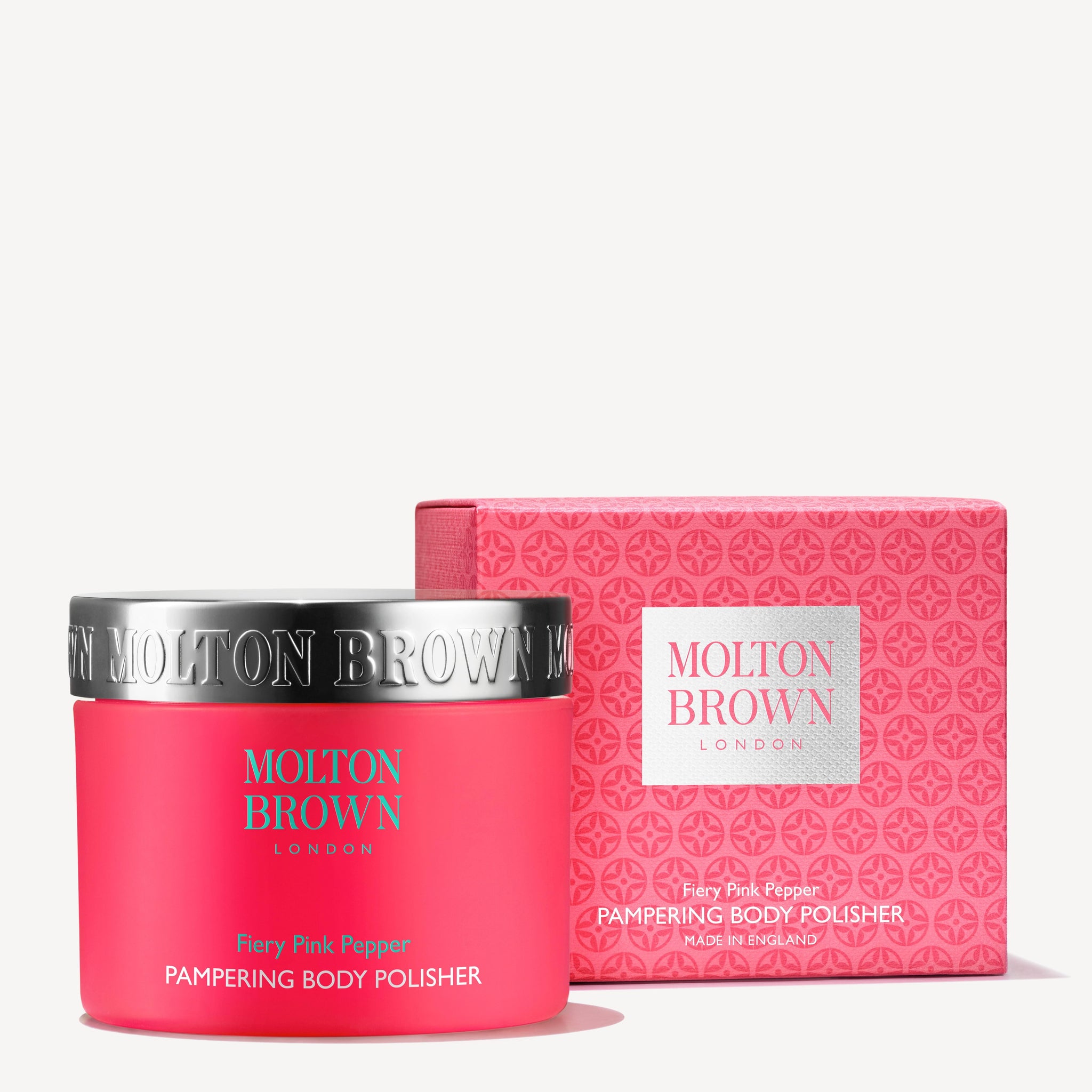 A pink container with a metallic lid and a matching box of MoltonBrown Cyprus Fiery Pink Pepper Pampering Body Polisher 275g, infused with exfoliating bamboo to enhance skin texture. Both items display the brand name and product details in white lettering.