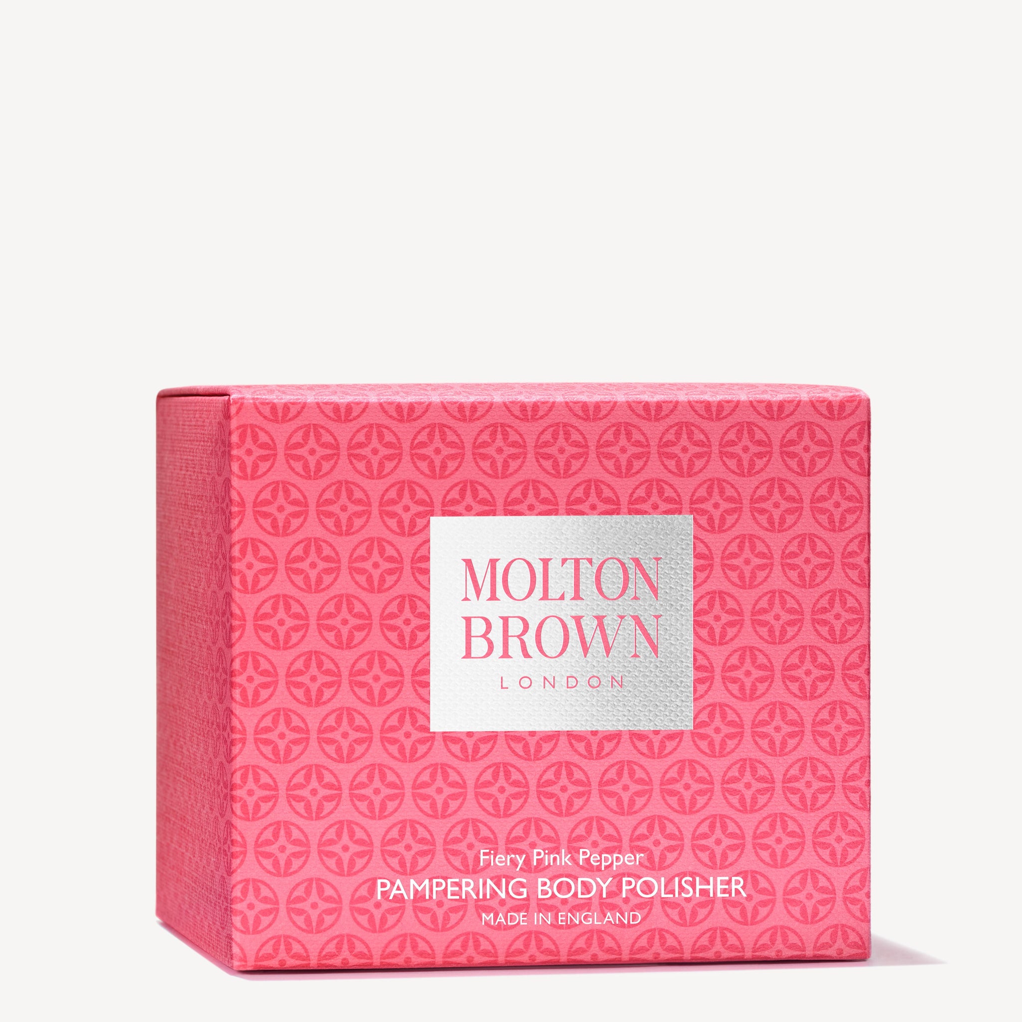 A pink square box with a repeating geometric pattern contains a Fiery Pink Pepper Pampering Body Polisher in a 275g size from MoltonBrown Cyprus, enriched with exfoliating bamboo to refine skin texture. The box features a white label displaying the brand name and product details.