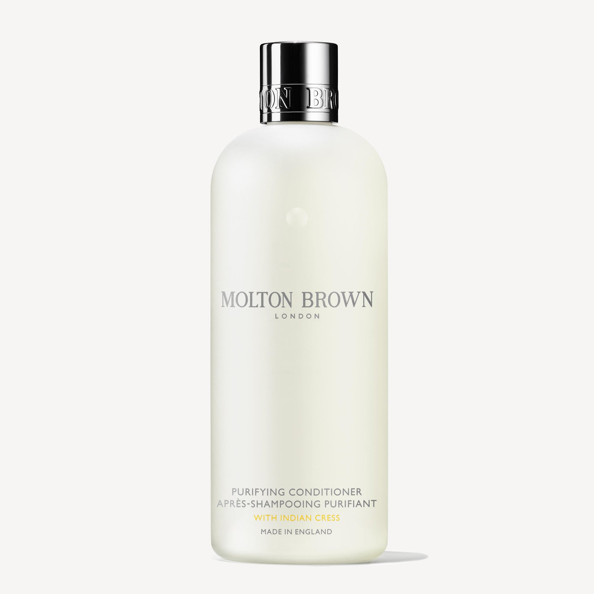 A white bottle of Molton Brown Cyprus Purifying Conditioner With Indian Cress 300ml is displayed. The text on the bottle features LONDON and Made in England in elegant fonts, with a simple, sleek design that exudes sophistication and is enhanced by subtle notes of honeysuckle.