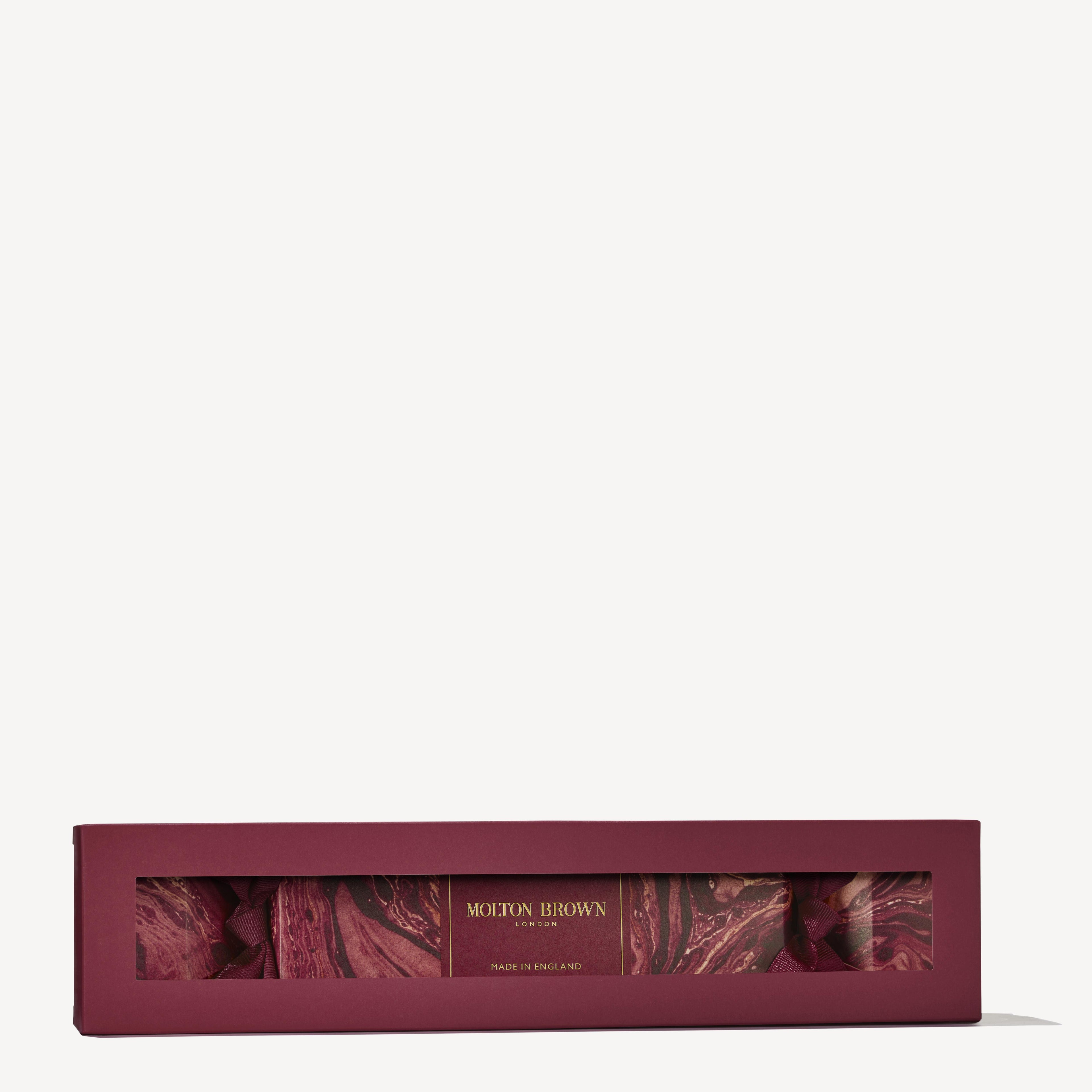 A rectangular burgundy box from MoltonBrown Cyprus, containing the Floral & Spicy Christmas Cracker shower gel products. The elegant packaging showcases a marbled design and includes a transparent window that reveals its contents, making it perfect for your Christmas table centerpiece. The phrase "Made in England" is elegantly printed on the box.