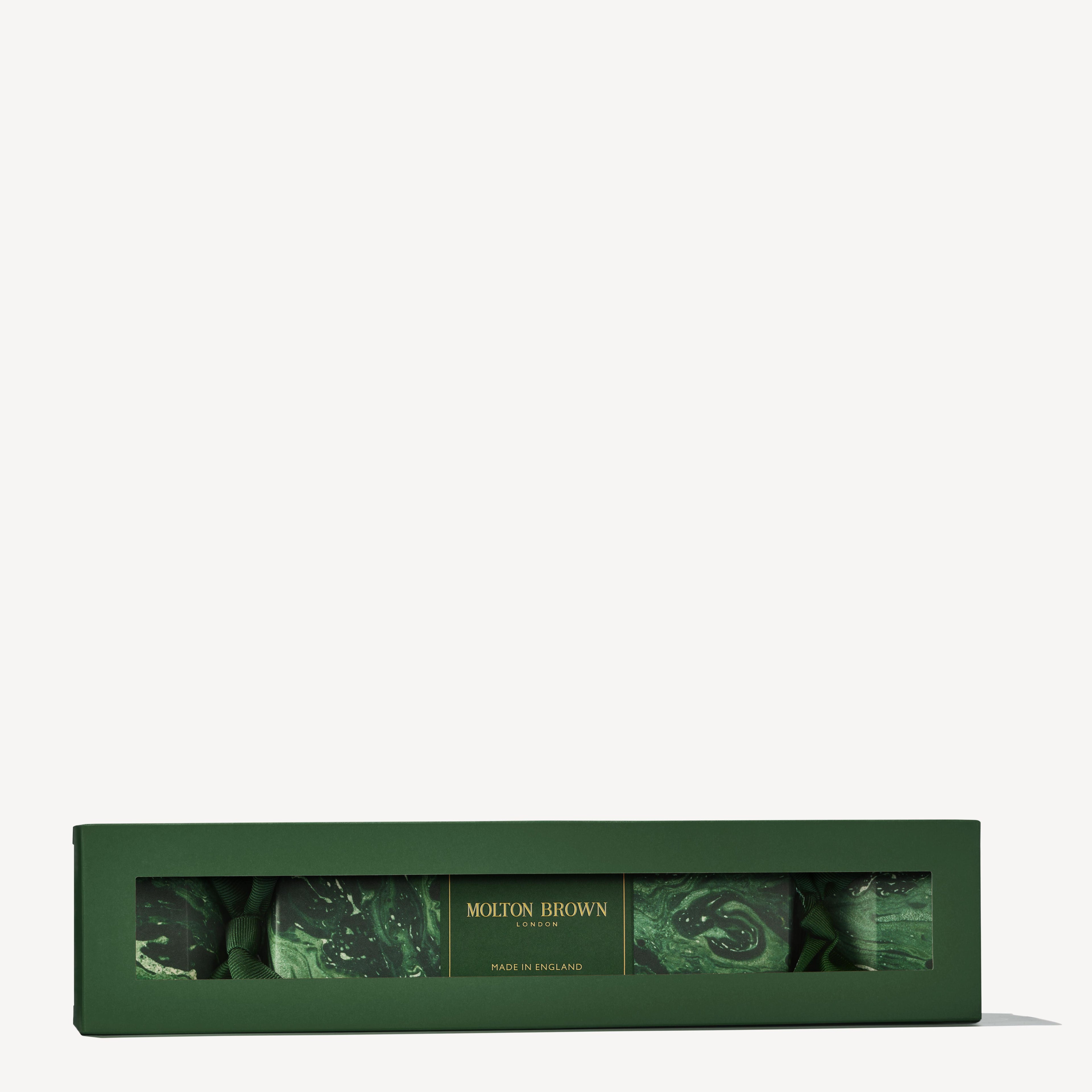 A festive, rectangular gift box in green houses an assortment of body washes from MoltonBrown Cyprus under the name Woody & Aromatic Christmas Cracker. The elegant marbled design on the packaging evokes a classic Christmas cracker aesthetic, set gracefully against a simple backdrop.