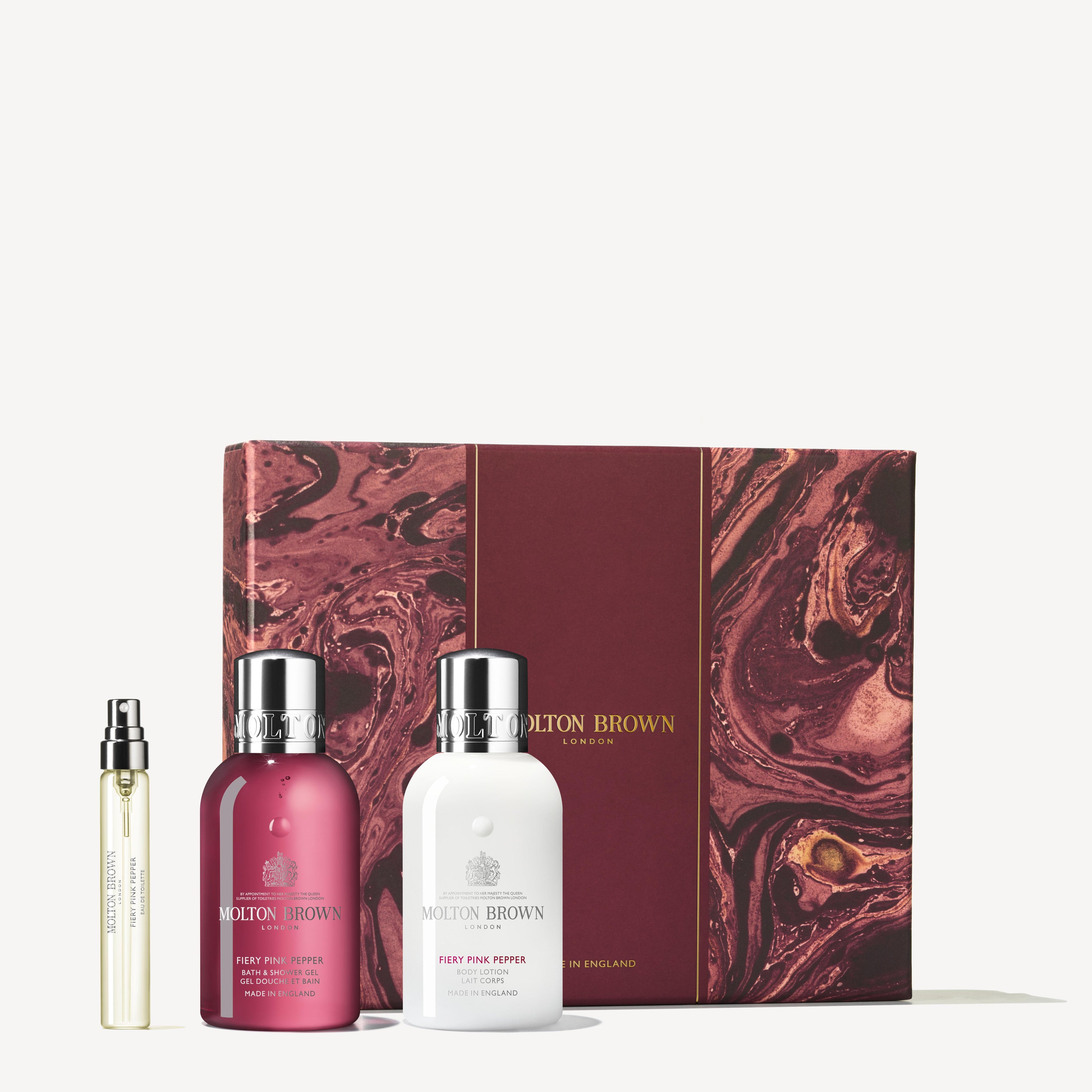 The MoltonBrown Cyprus Fiery Pink Pepper Travel Gift Set showcases a maroon and white body wash with a delicate marbled design on the package. It also includes a sleek spray bottle of Eau de Toilette infused with pink pepper, all beautifully presented against a neutral backdrop.