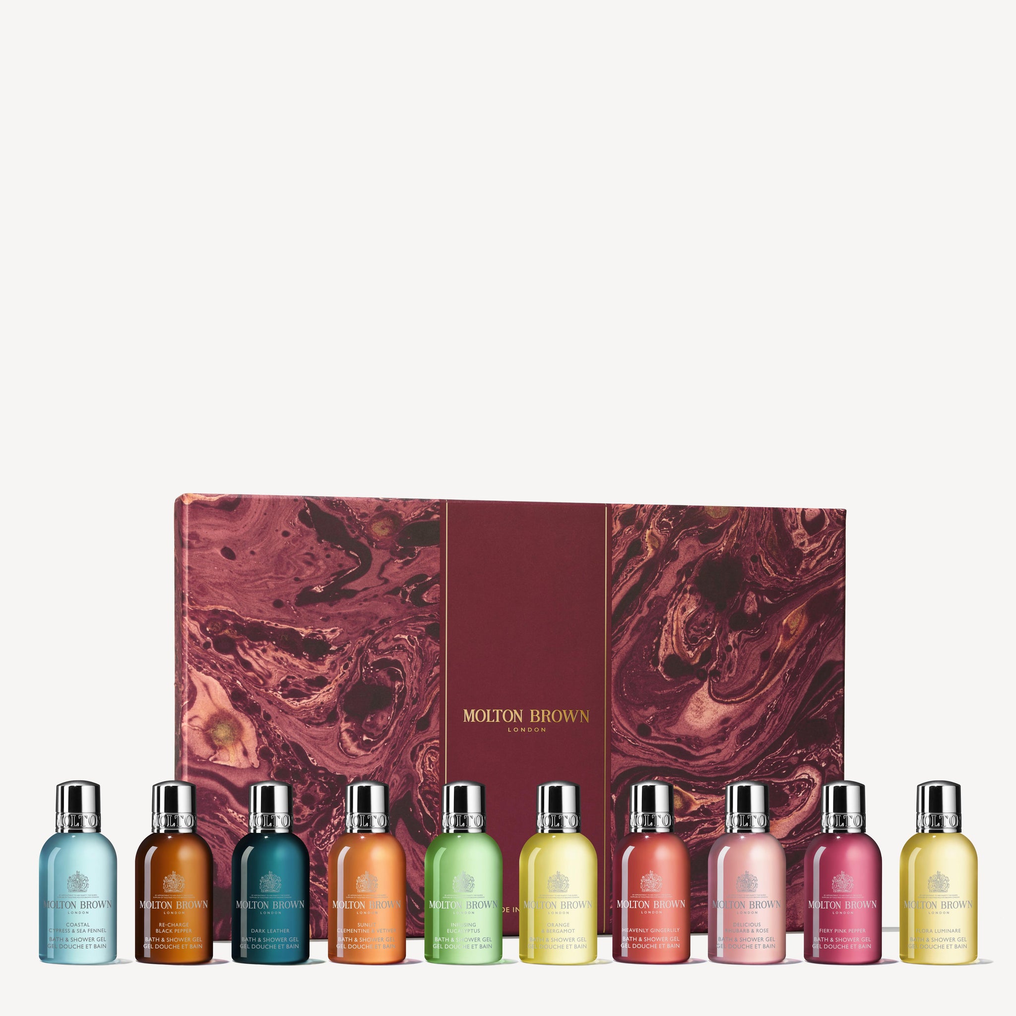 The Stocking Filler Gift Set by MoltonBrown Cyprus features a collection of body washes, each boasting distinct fragrance concentrations, beautifully arranged in front of a maroon gift box adorned with a marbled design. The bottles display an assortment of vibrant colors such as blue, orange, green, yellow, and pink.