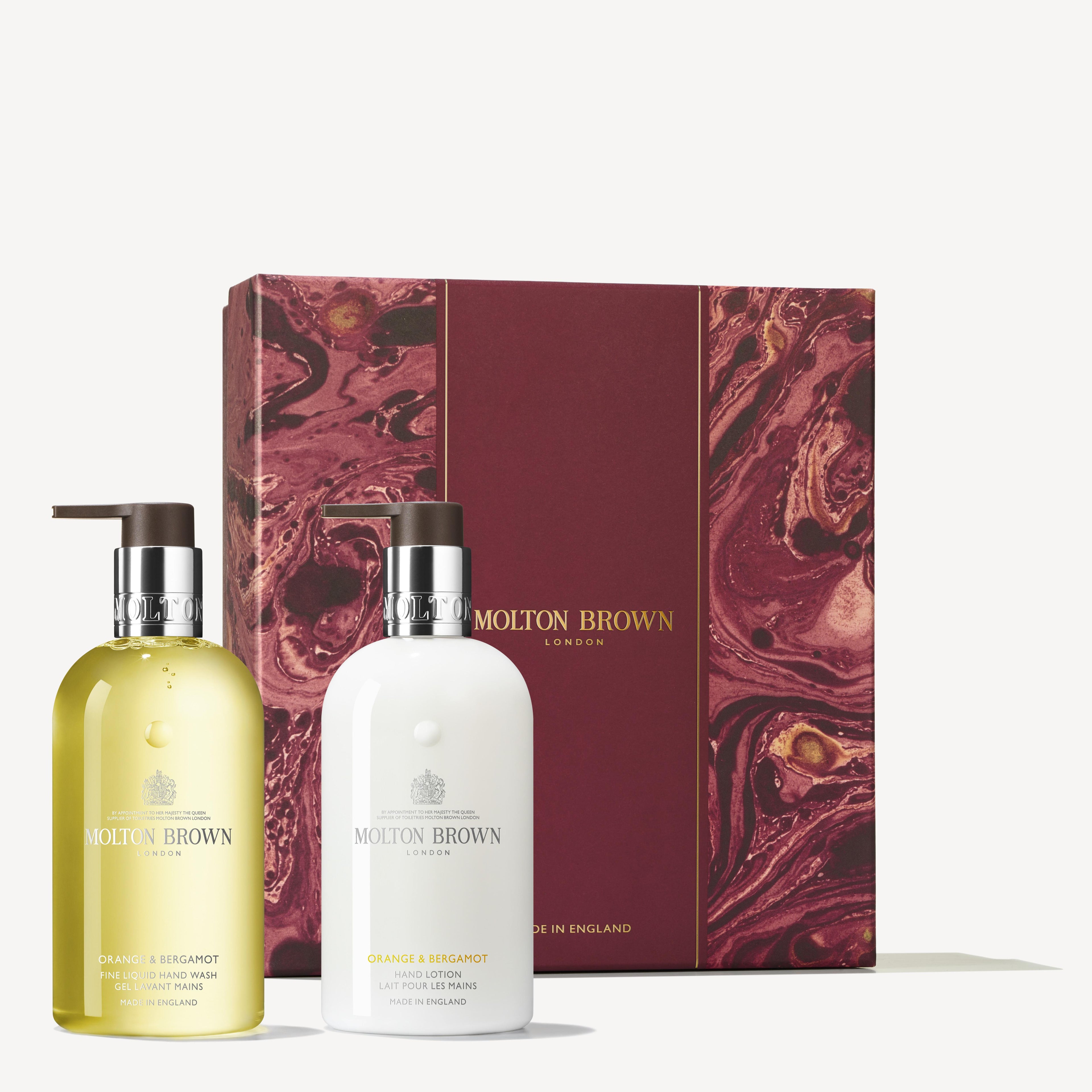 A MoltonBrown Cyprus gift set features a maroon box with gold accents and contains two bottles: one with a yellow-orange liquid, labeled Orange & Bergamot Bath & Shower Gel, and another with white cream, labeled Orange & Bergamot Body Lotion.