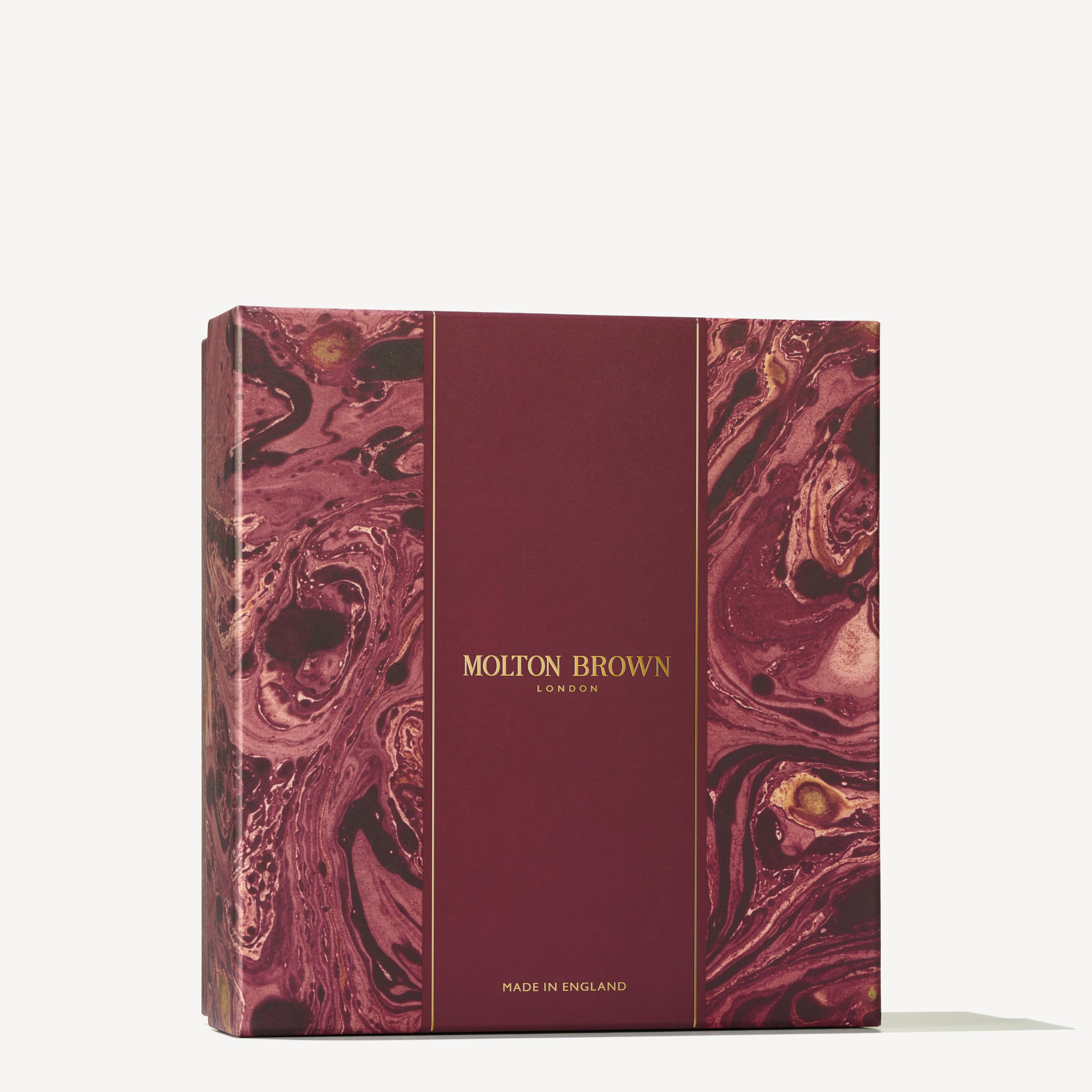 A square box with a marbled burgundy and gold design showcases the text MoltonBrown Cyprus in gold lettering on a central stripe. Below, it states "Made in England." The elegant swirls hint at the luxury of citrus hand care within, infused with Sevillian orange and neroli as part of the Orange & Bergamot Hand Care Gift Set.