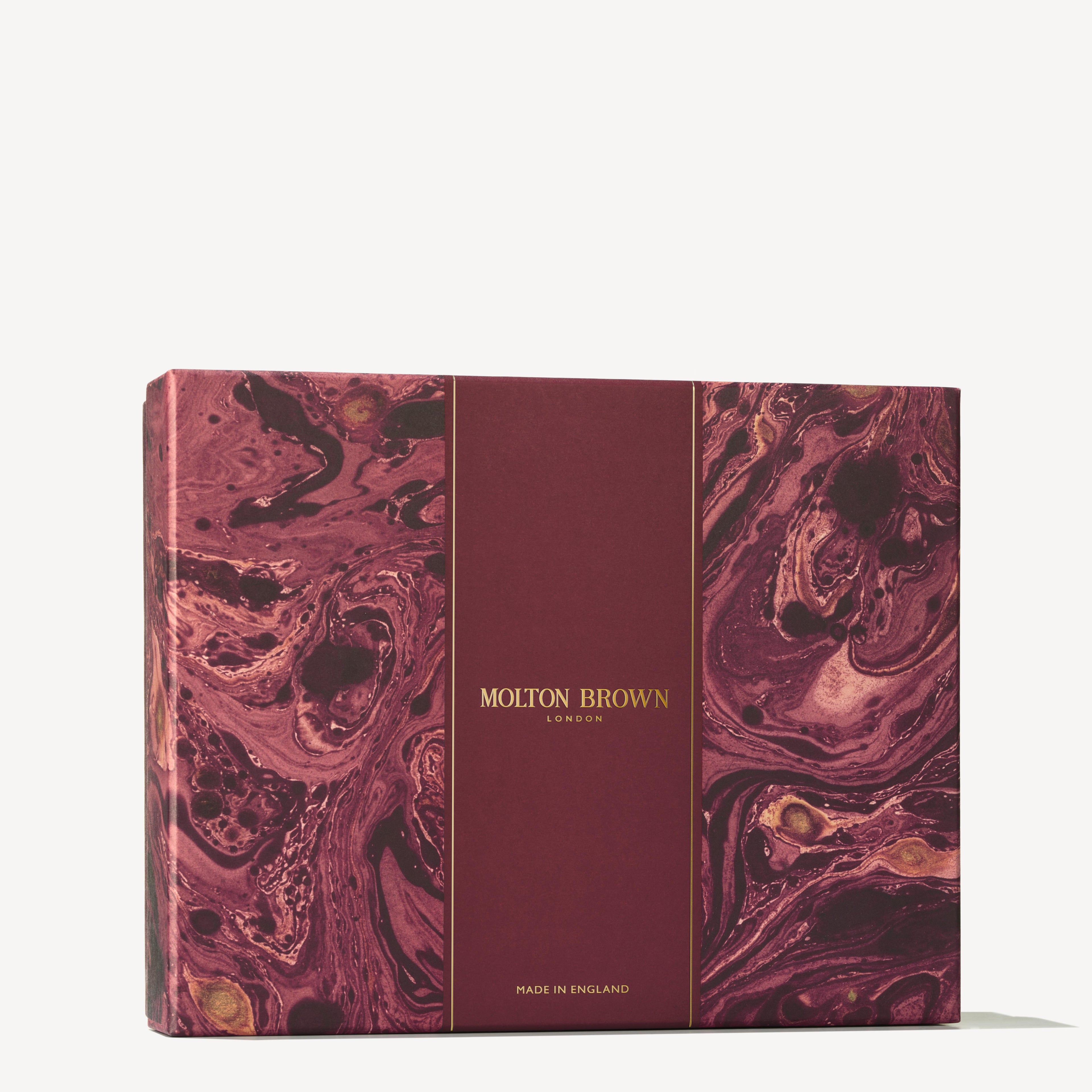 A rectangular gift box showcasing a marbled burgundy design is adorned with a central band that reads "MoltonBrown Cyprus" in gold, evoking their citrus floral-fruity aromatic scents. The phrase "Made in England" is elegantly inscribed at the bottom of the box, which is set against a plain off-white background.