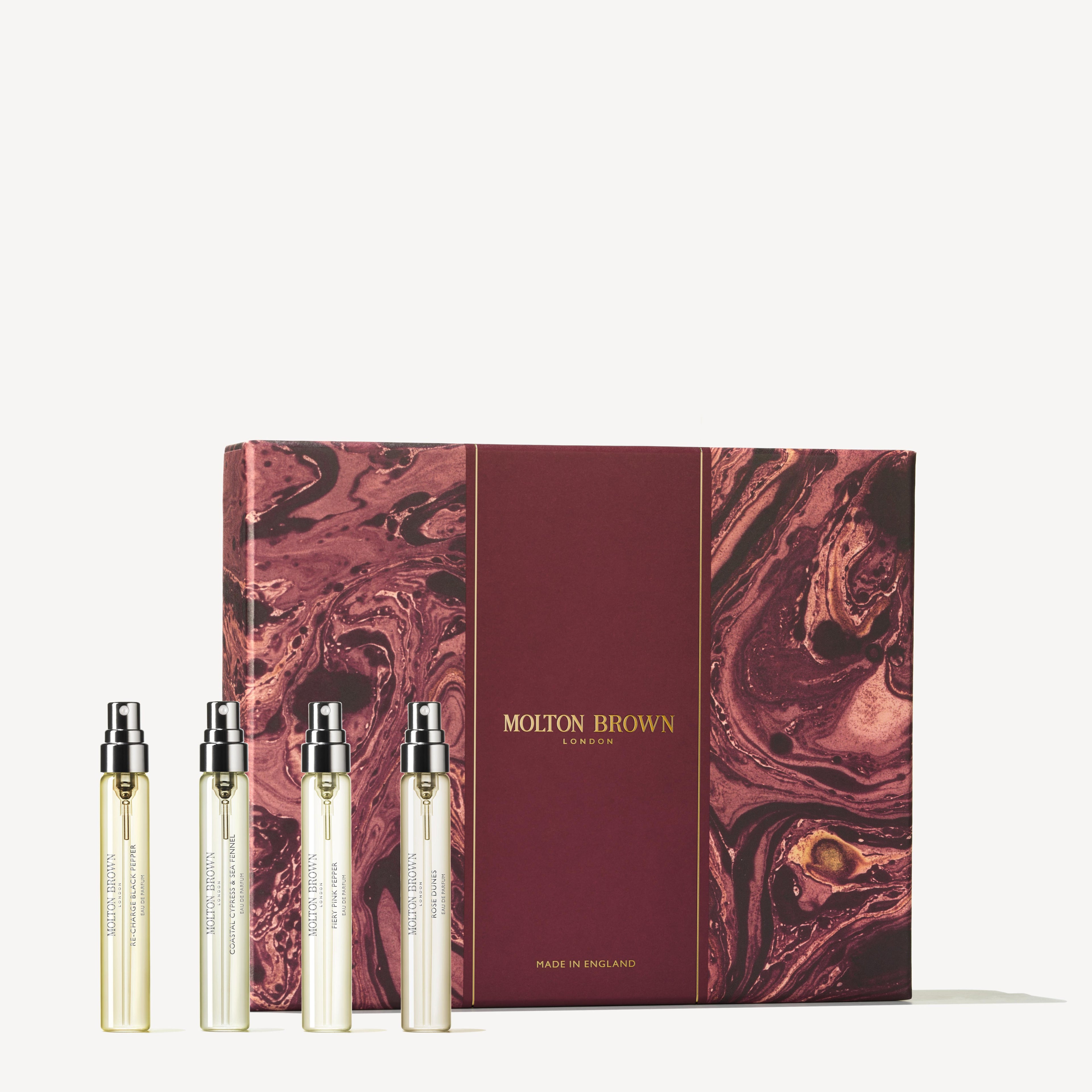 A Woody & Floral Fragrance Discovery Set from MoltonBrown Cyprus features four bestselling Eau de Parfum slim spray bottles elegantly displayed next to a maroon and gold box with a marbled design. The text on the box reads "Molton Brown London Made in England.