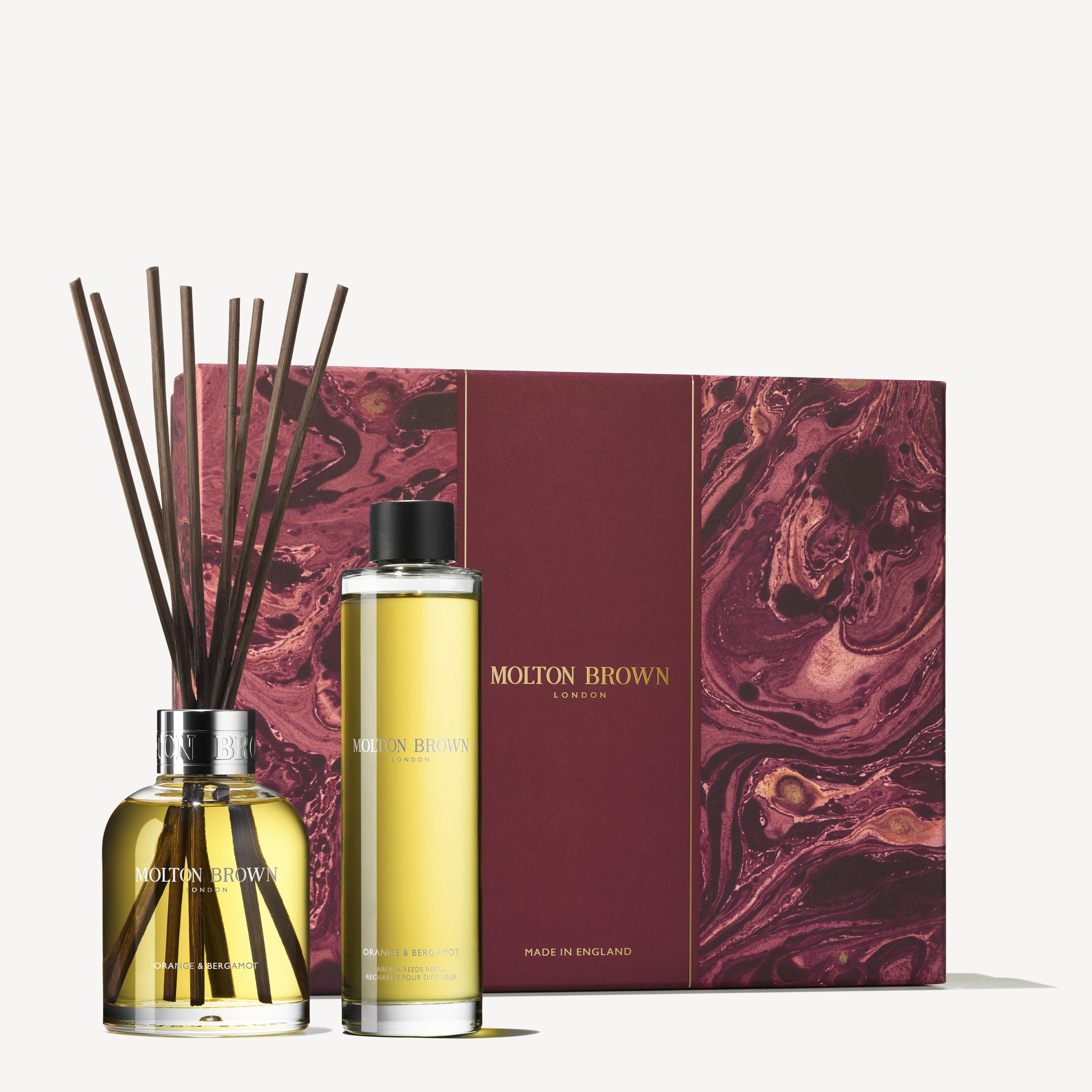 A MoltonBrown Cyprus Orange & Bergamot Home Fragrance Gift Set, featuring a room diffuser with reeds and a bottle of refill oil infused with a citrus scent. The packaging is designed in a rich maroon color with gold accents and features a marbled pattern.