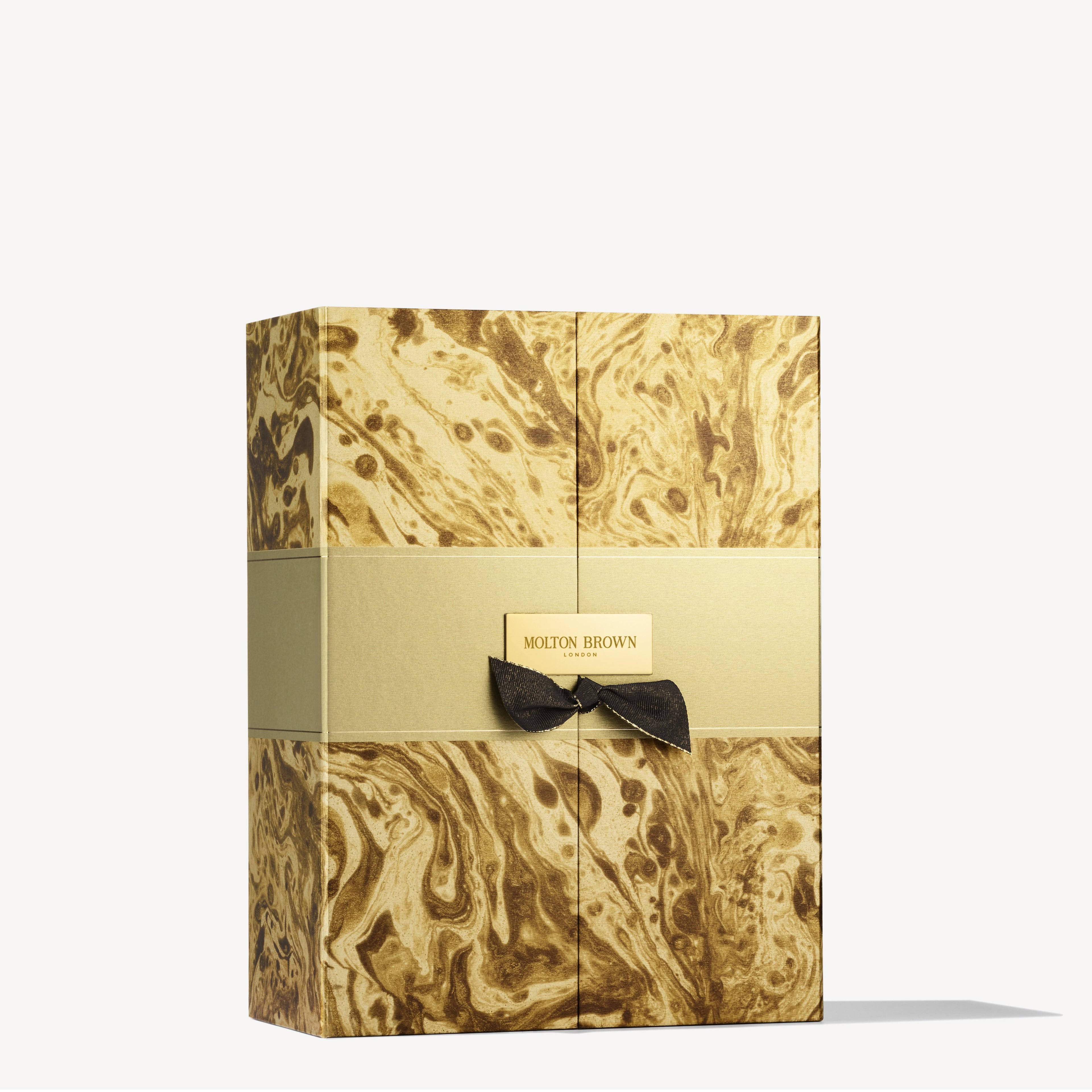 The MoltonBrown Cyprus Advent Calendar is a luxurious gift box adorned with an elegant marbled gold and beige design, inspired by a marble artist. It features a black bow and central label, making it look exquisite. This Limited Edition product sits on a light surface against a plain background, ready to unveil its fragrant surprises.