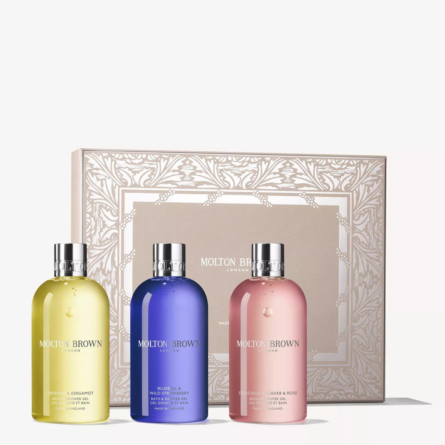 Three MoltonBrown Cyprus Floral & Fruity Body Care Gift Set bottles in yellow, blue, and pink stand before a beige floral-patterned gift box featuring the brand’s logo.