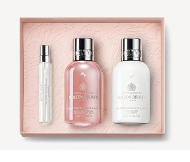 Explore an ideal Mother's Day gift with the Molton Brown Cyprus Delicious Rhubarb & Rose Travel Gift Set. This set includes a compact white cylindrical spray bottle, a pink liquid bottle, and a white lotion bottle, all beautifully packaged in a light pink box featuring a delicate floral-fruity design.