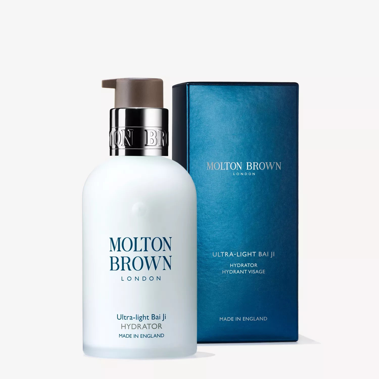 A white bottle of Molton Brown Cyprus Ultra-light Bai Ji Hydrator, infused with bai ji extract, has a pump dispenser and is next to a coordinating blue box. Both display the brands name prominently. The packaging declares Made in England on a clean white backdrop.