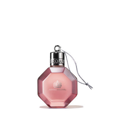 A pink, octagonal perfume bottle from MoltonBrown Cyprus, styled as the Delicious Rhubarb & Rose Festive Bauble 75ml, features a silver cap adorned with an engraved "BROWN" and a small chain. The bottle, reminiscent of a festive decoration, showcases a delicate floral design infused with grapefruit notes. It stands upright against a plain white background.