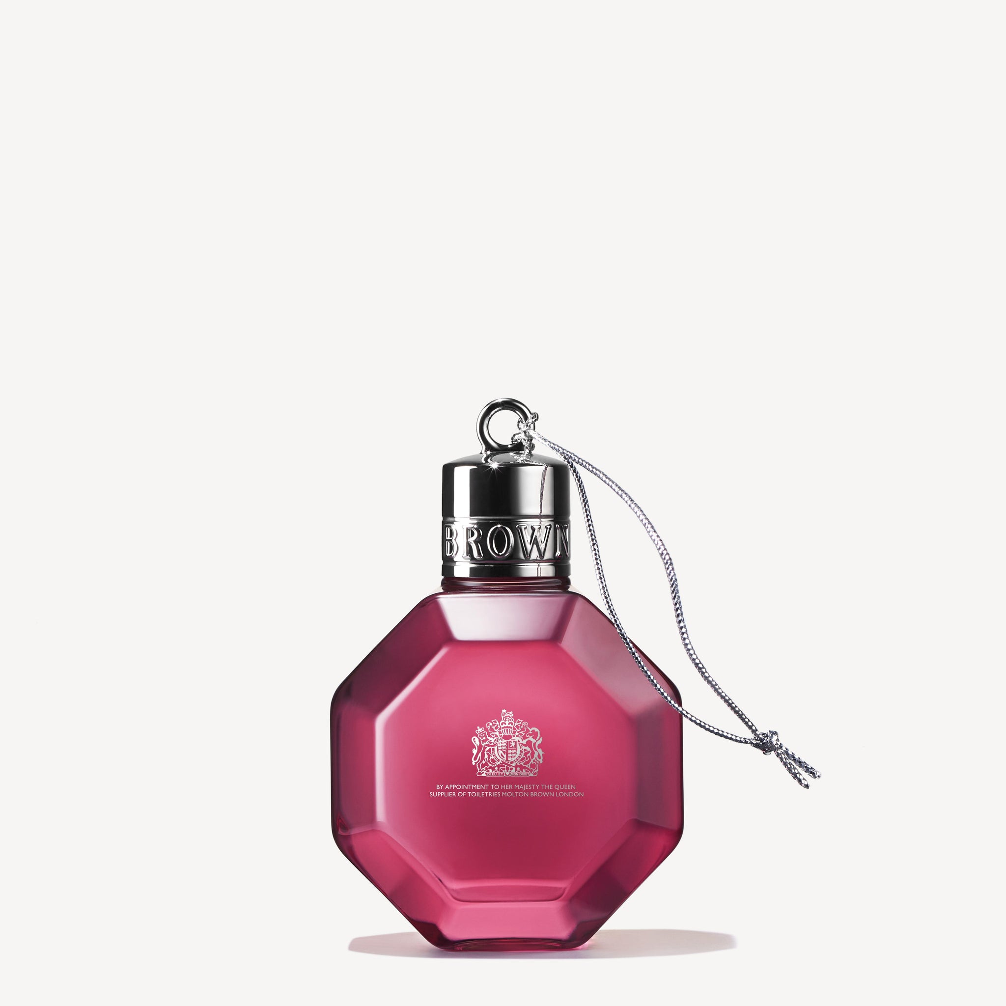 The Fiery Pink Pepper Festive Bauble by MoltonBrown Cyprus is a pink, octagonal perfume bottle adorned with a silver cap and a small dangling cord, resembling the charm of a festive bauble. This bottle showcases intricate design details and reflective accents, set against a plain white background.