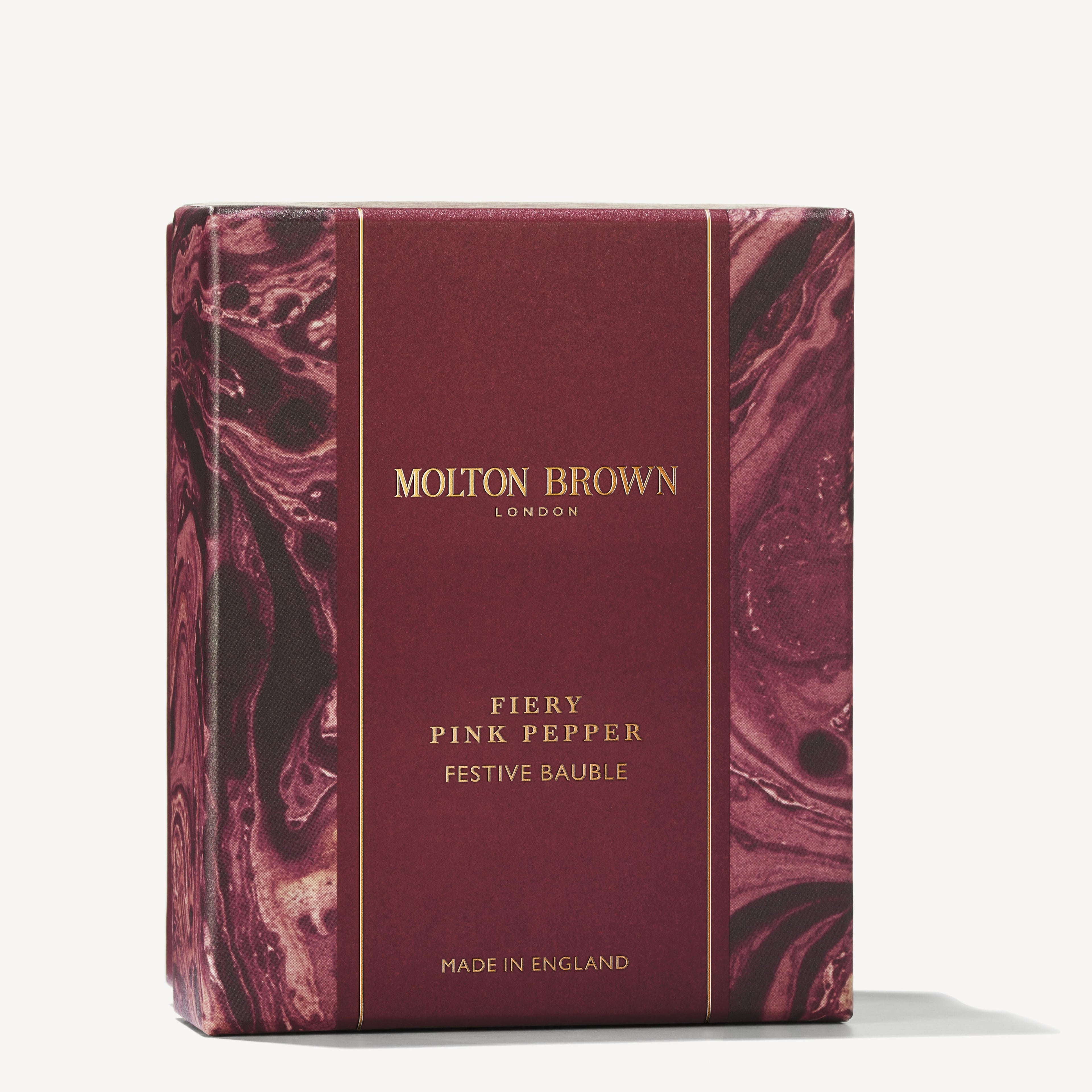 The packaging for MoltonBrown Cyprus' Fiery Pink Pepper Festive Bauble shower gel is designed in a maroon box with swirling patterns and gold text. The brand's name and product details are elegantly displayed, with "Made in England" noted at the bottom.